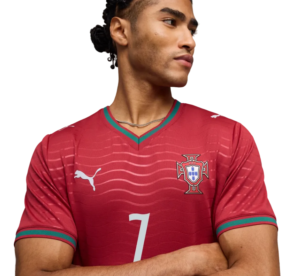 A man wears a red Puma Portugal soccer jersey with the number 7, featuring wavy patterns and green trim, posing with arms crossed against a black background.