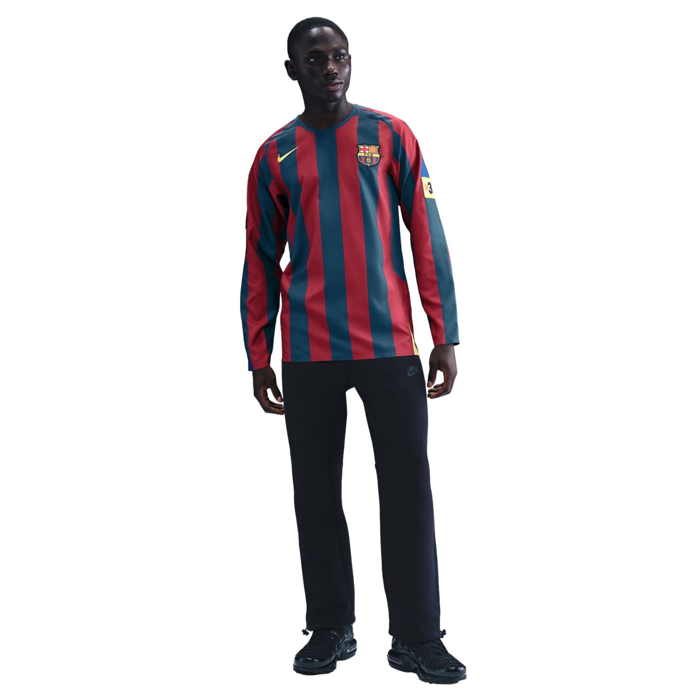 A young man models a long-sleeved FC Barcelona soccer jersey with red and blue vertical stripes, paired with black athletic pants and black sneakers against a solid black background.
