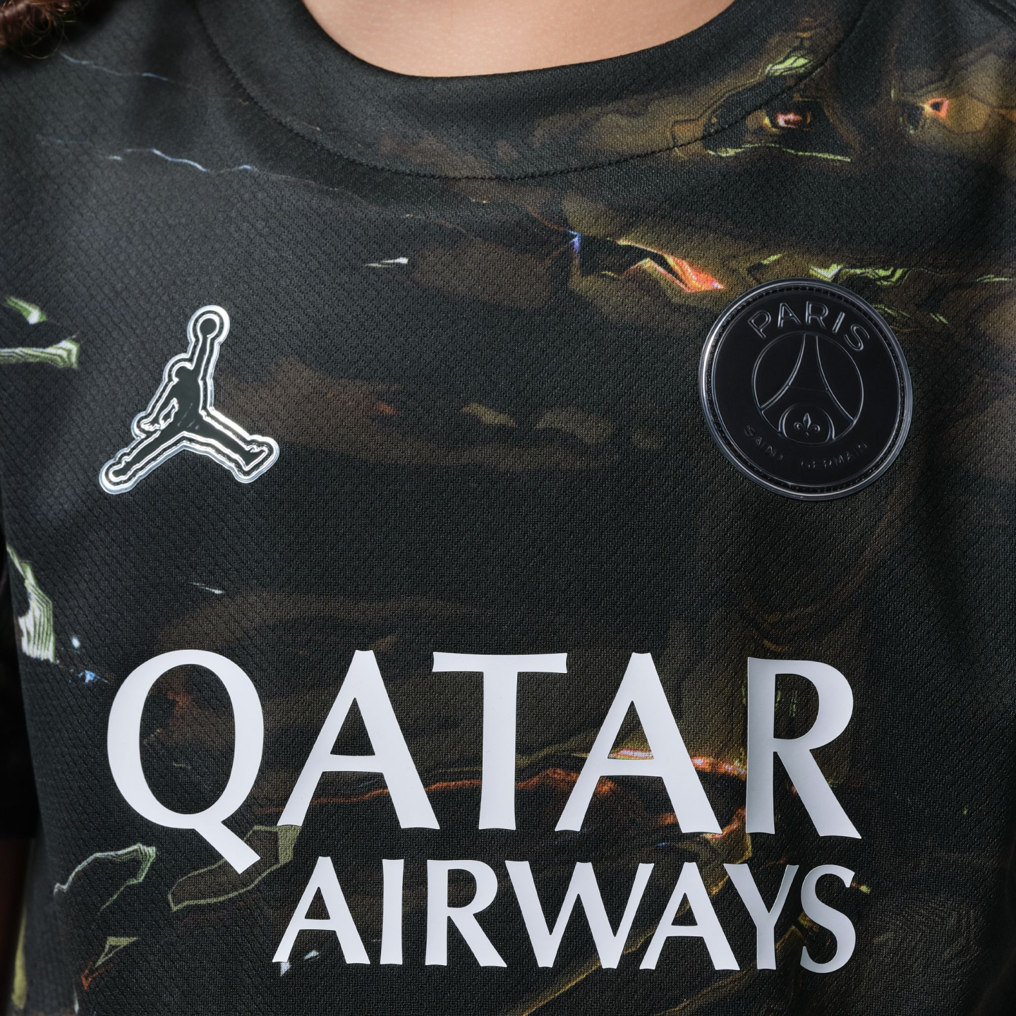 Close-up of a dark patterned Paris Saint-Germain jersey with silver Jumpman logo, black club crest, and white "QATAR AIRWAYS" text.