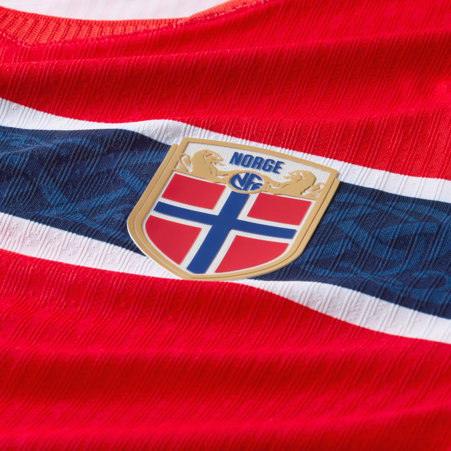 Close-up of a red Norway football jersey with white and blue stripes and a gold crest featuring the Norwegian flag and the word "NORGE."