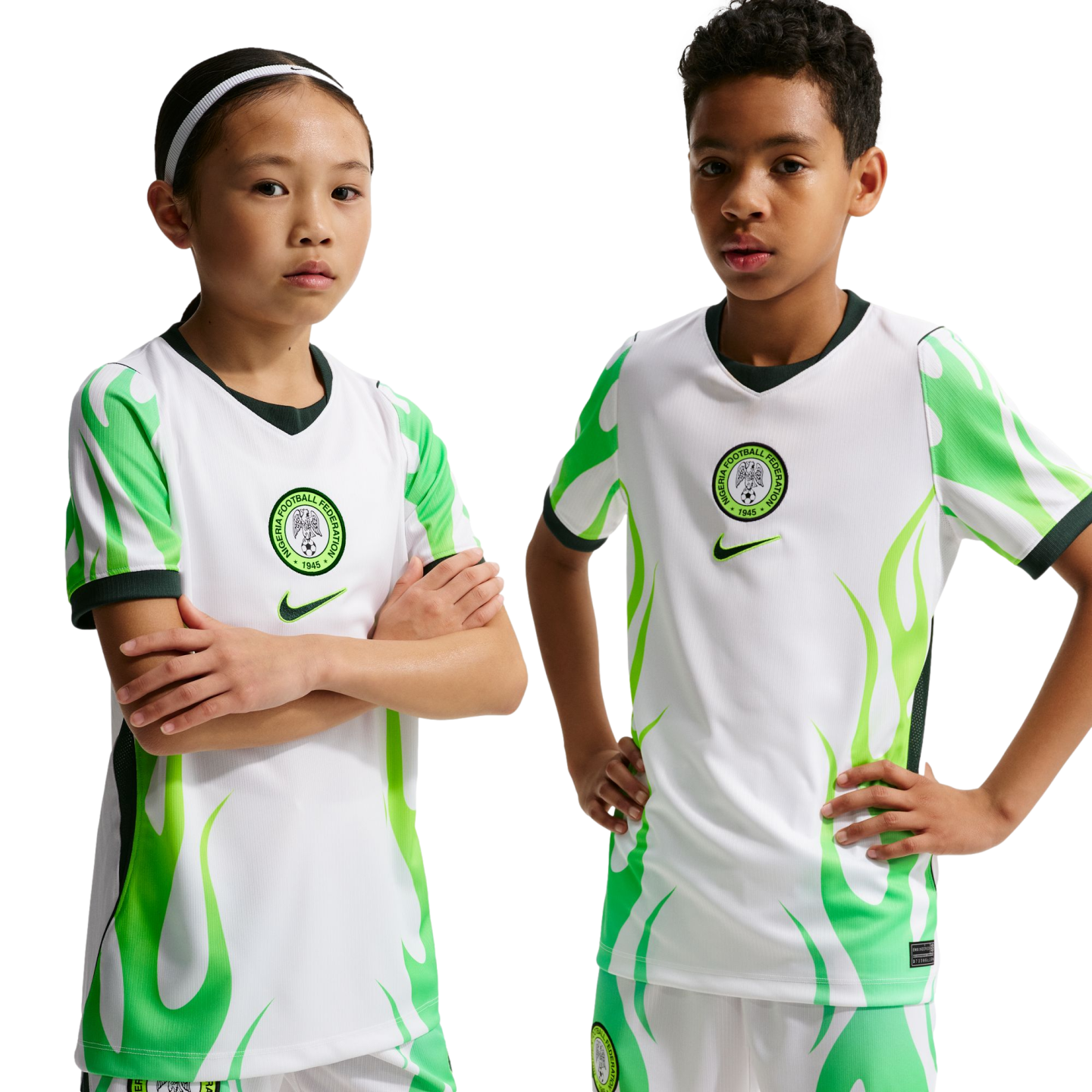 Two children, one with arms crossed and one with hands on hips, wear Nigeria national soccer jerseys featuring white and green flame designs against a black background.