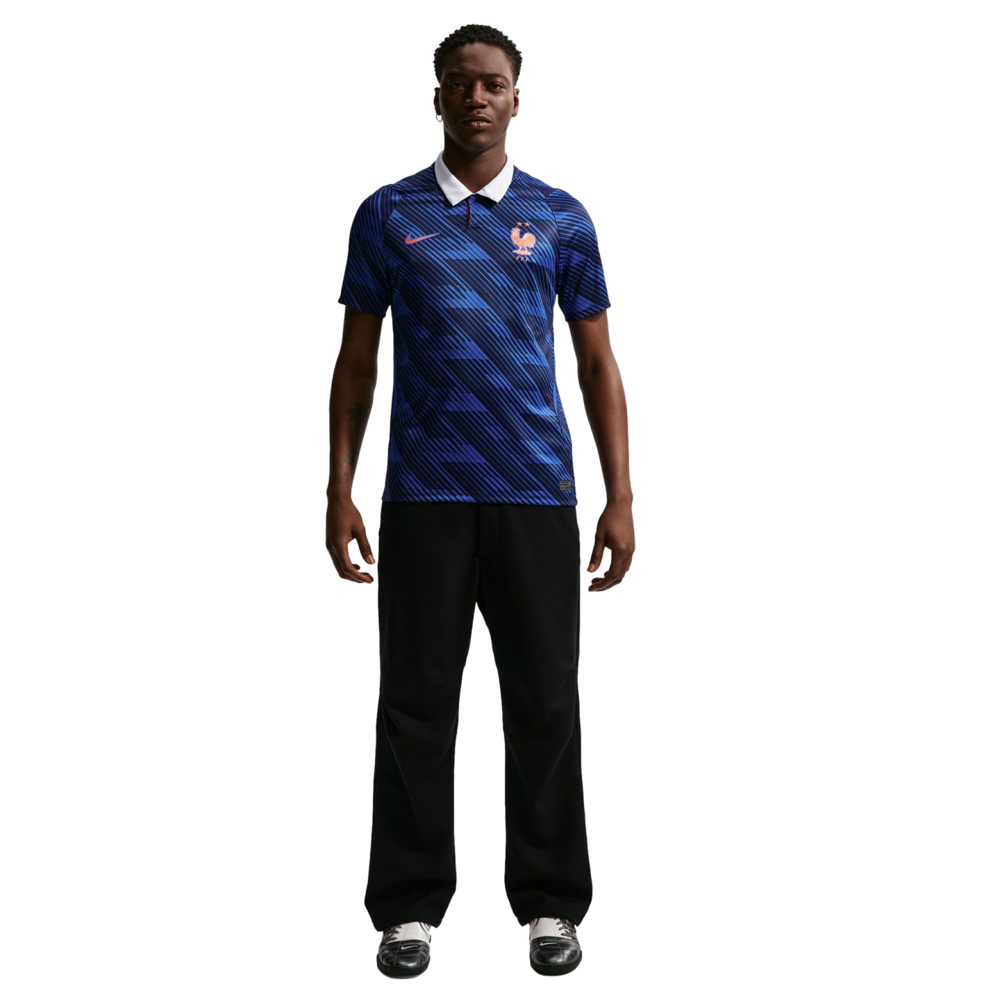 A man modeling a blue patterned France soccer jersey with a white collar, black trousers, and athletic shoes against a black background.