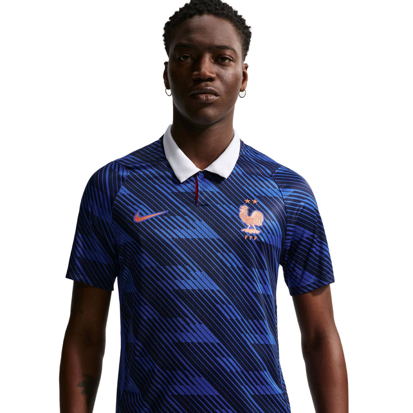 A man wearing a blue Nike France football jersey with a white collar and diagonal patterns, featuring a gold rooster crest and two stars, set against a black background.