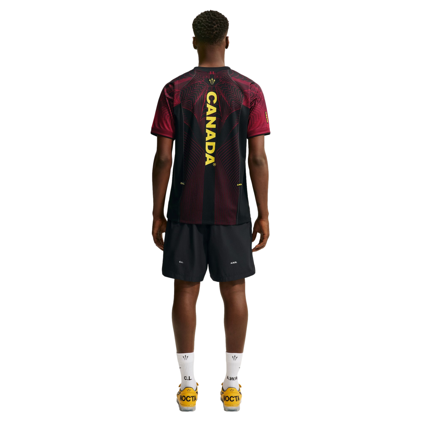 Rear view of a man wearing a black and red jersey with "CANADA" on the back, black shorts, and yellow shoes against a white background.