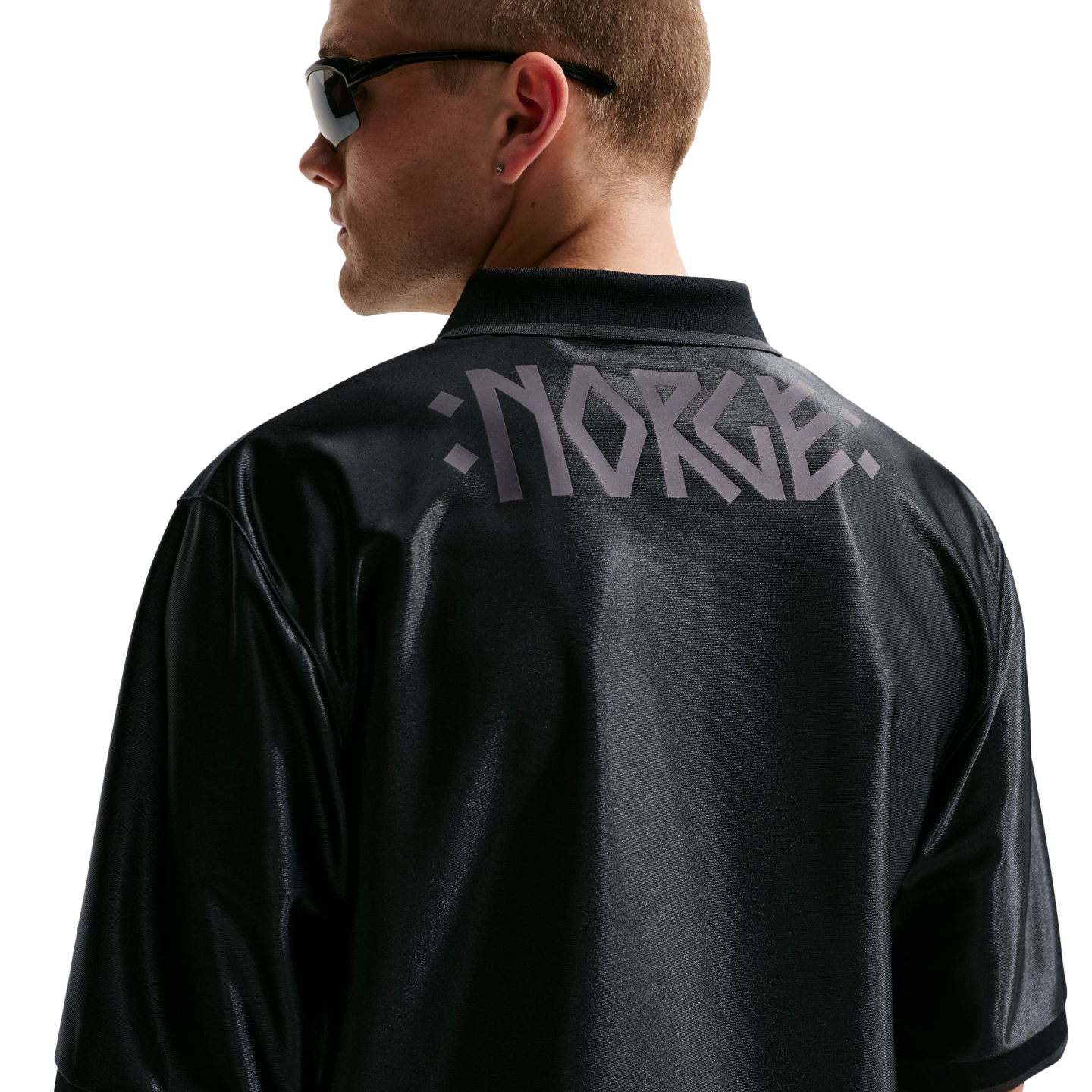 Back view of a man in a black shiny jersey with "NORGE" in grey stylized letters across the shoulders. He wears sunglasses and looks left against a white background.