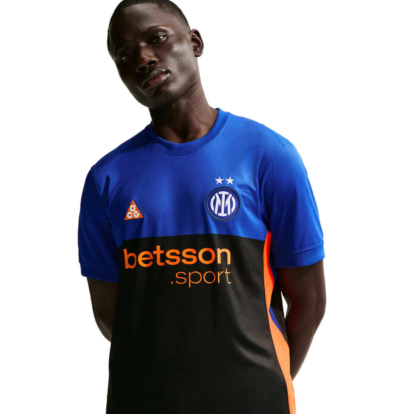 A man in a blue and black Inter Milan training jersey with orange "betsson.sport" and ACG logos. He poses with hands behind his back against a black background.