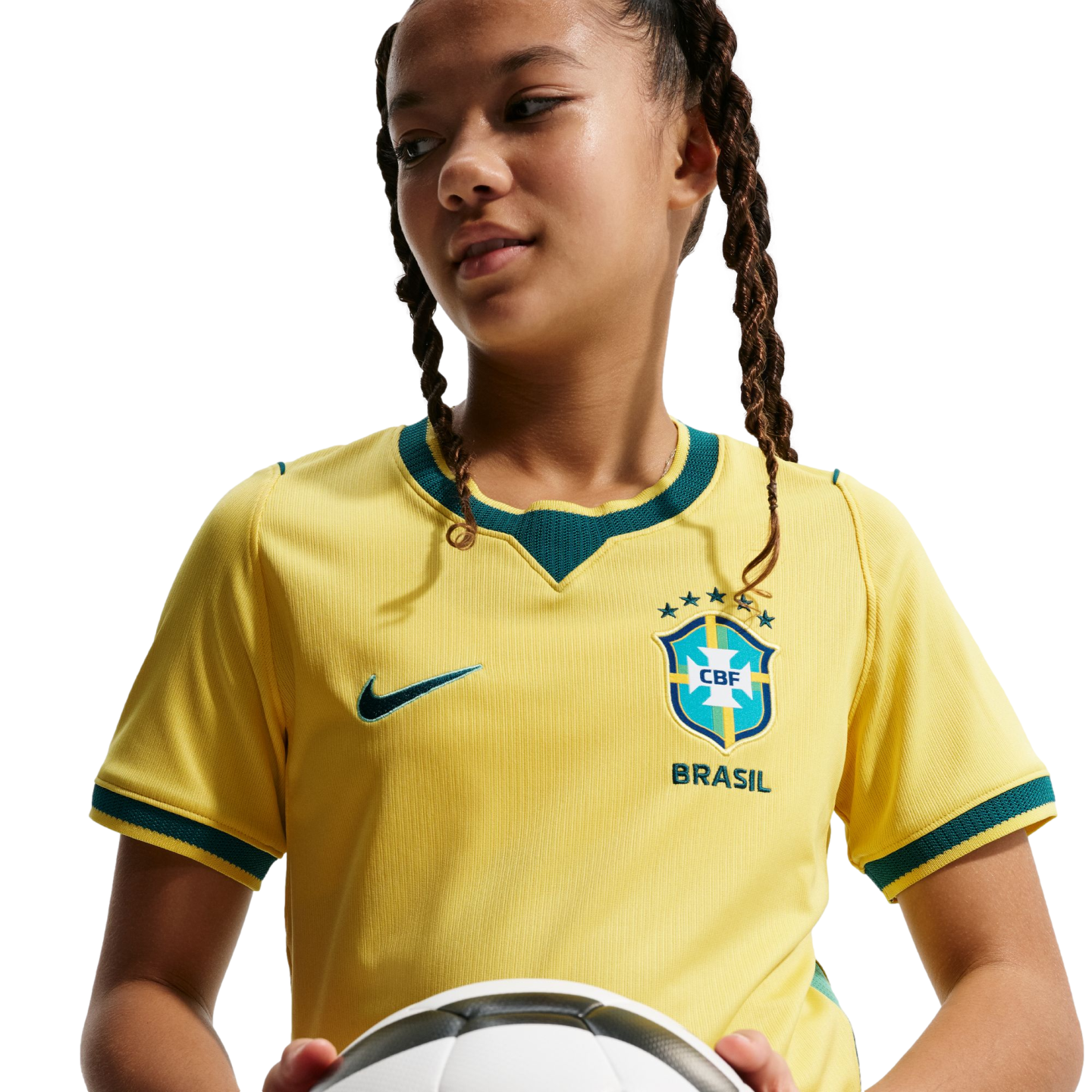A person with braided hair wearing a yellow Brazil soccer jersey and holding a soccer ball against a black background.