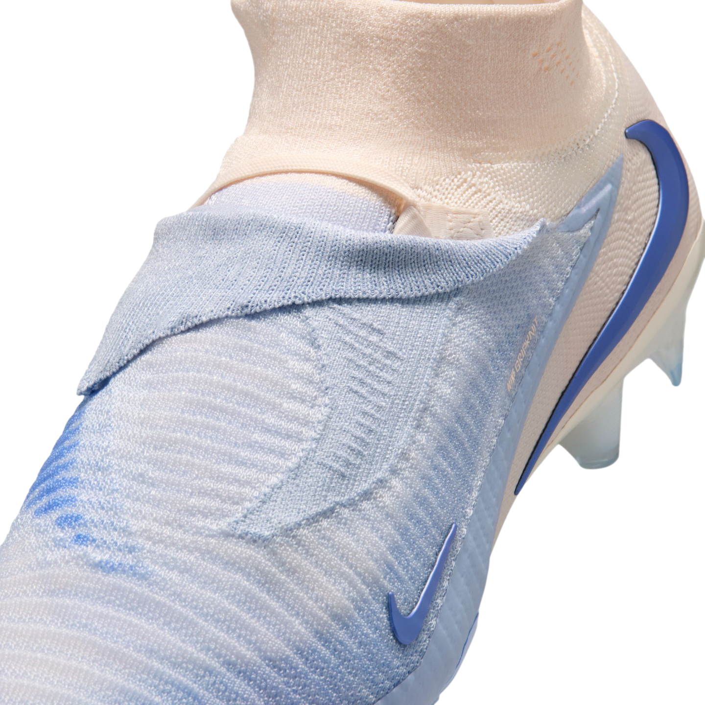 Close-up of a light blue and peach Nike soccer cleat with a textured, laceless knit upper and a sock-like collar against a black background.
