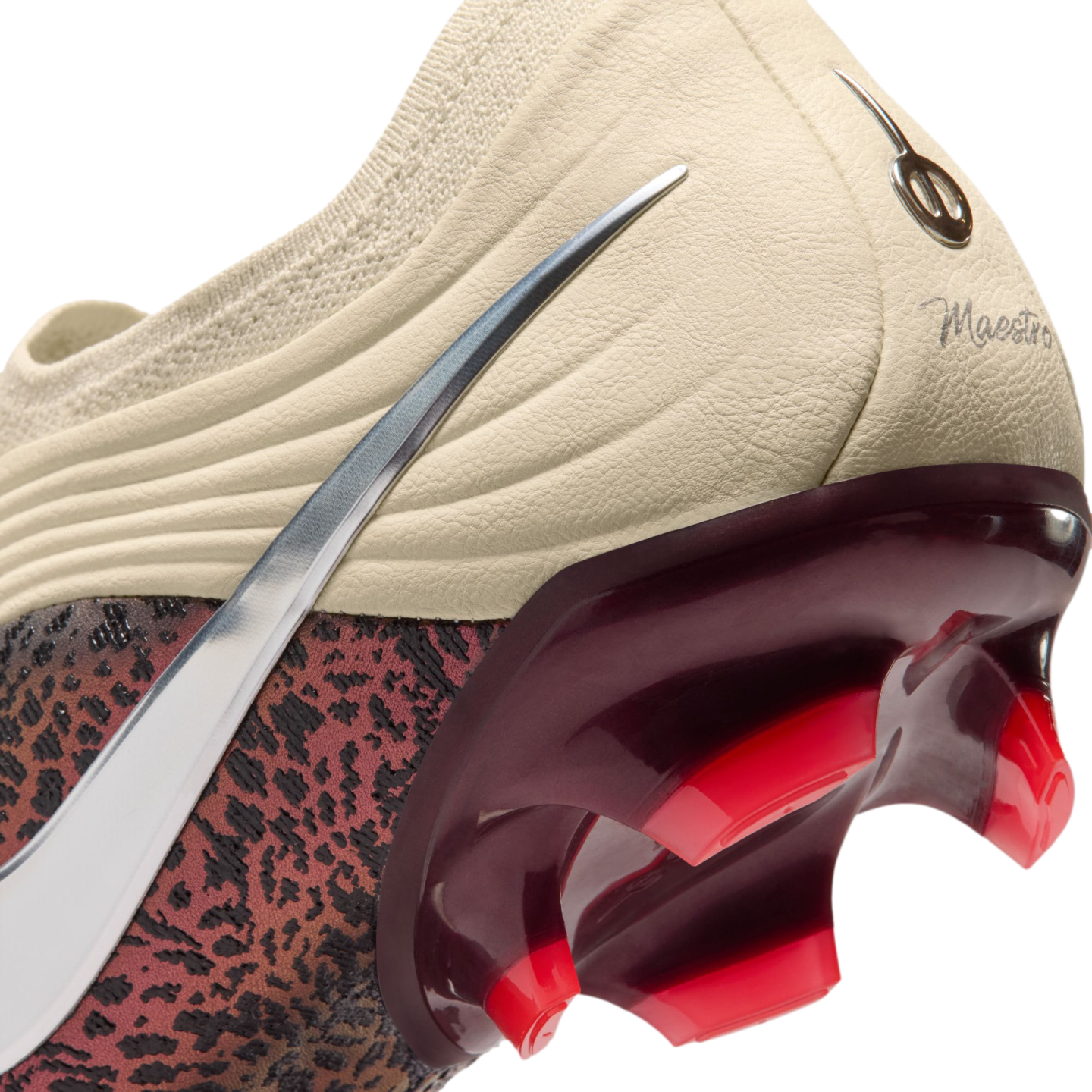 A close-up view of the heel and soleplate of a Nike soccer cleat against a black background. The upper features a cream-colored textured heel with a script "Maestro" inscription and a silver metallic Nike Swoosh. A glossy, deep-red translucent heel counter transitions into bright red studs. The lower side of the boot displays a dark red and black leopard-like print.