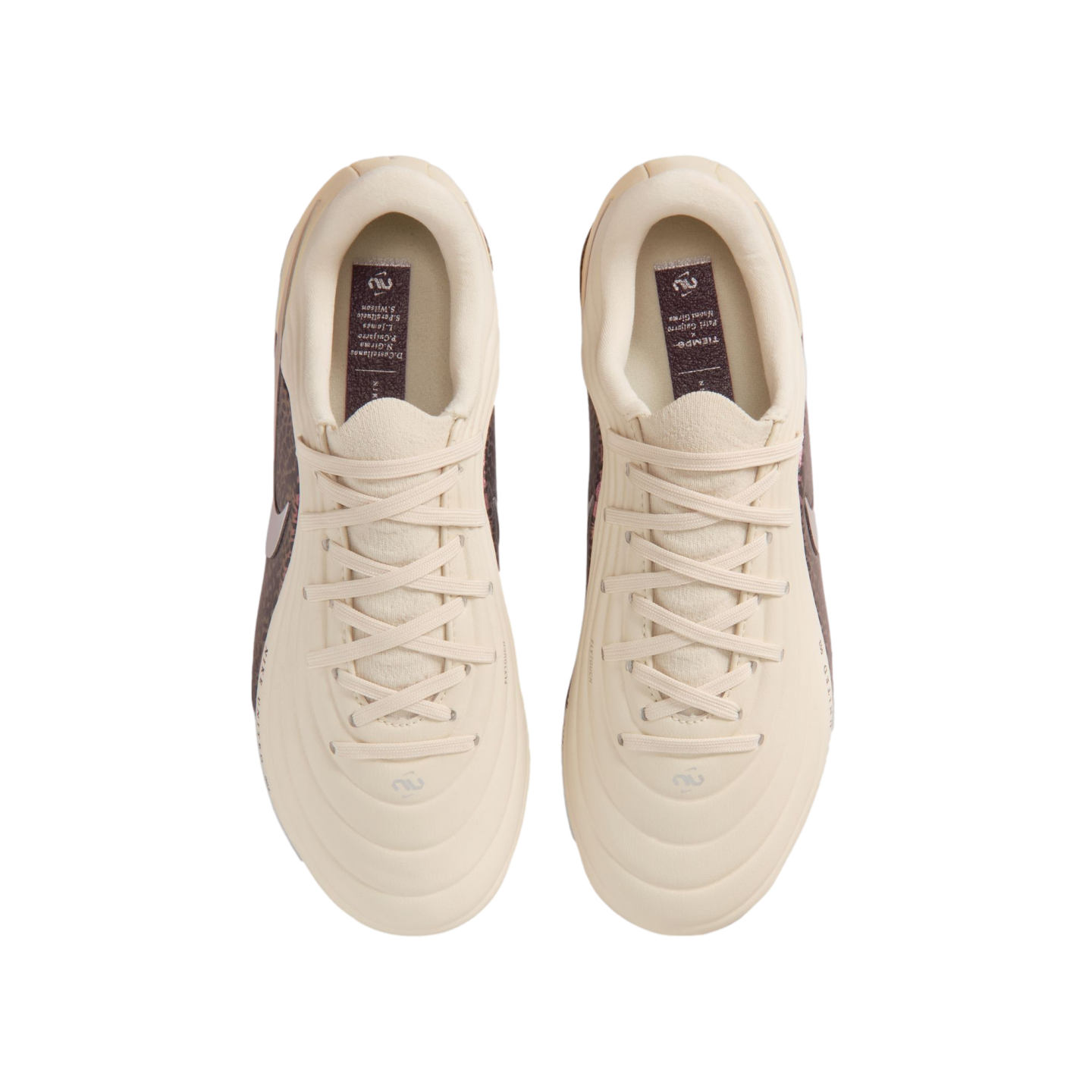 A top-down view of a pair of cream-colored Nike Tiempo soccer cleats centered against a black background. The shoes feature matching cream laces and a quilted, textured upper. Inside each shoe, a dark purple insole displays the "Tiempo" name and a list of other names in white text.