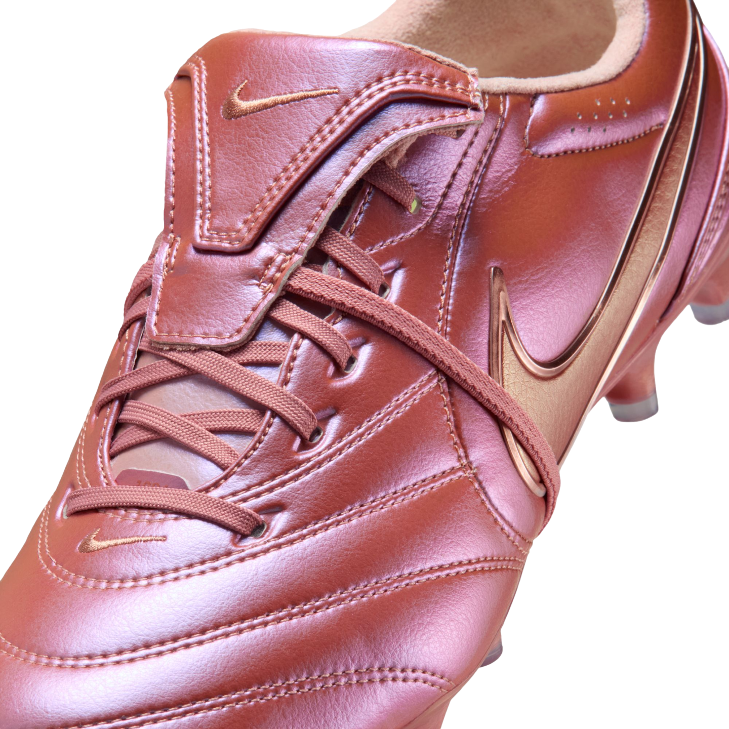Close-up of a metallic copper Nike soccer cleat with leather texture, matching laces, and swoosh logos against a black background.