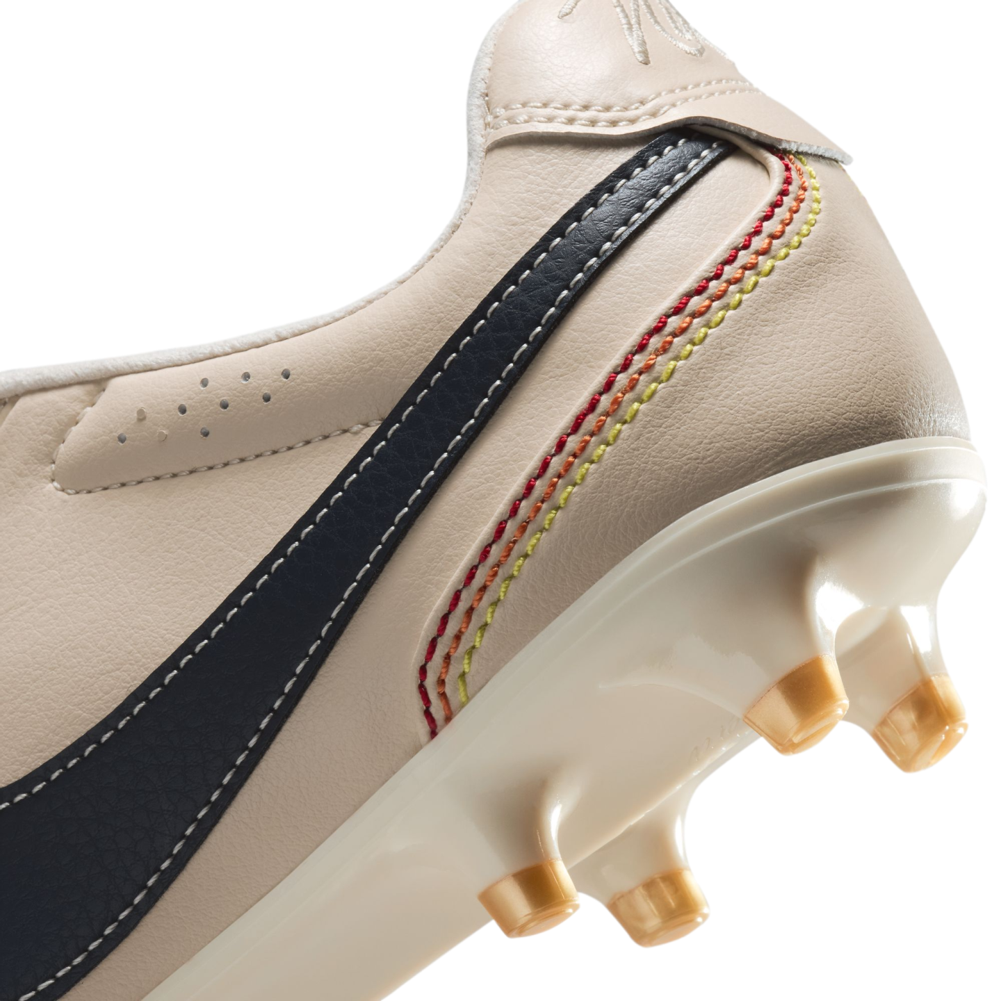 A close-up view of the heel and sole of an off-white leather soccer cleat. The shoe features a dark blue stripe with white stitching and five decorative, curved rows of stitching in a red, orange, and yellow gradient. The glossy white sole plate has translucent, yellowish conical studs, all set against a solid black background.
