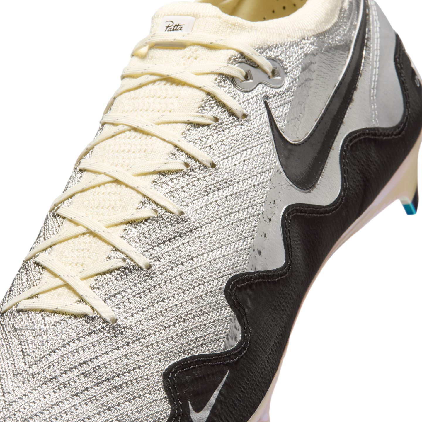 Close-up of a silver and cream Nike x Patta soccer cleat featuring a textured metallic upper and a wavy black side panel with a Nike swoosh.