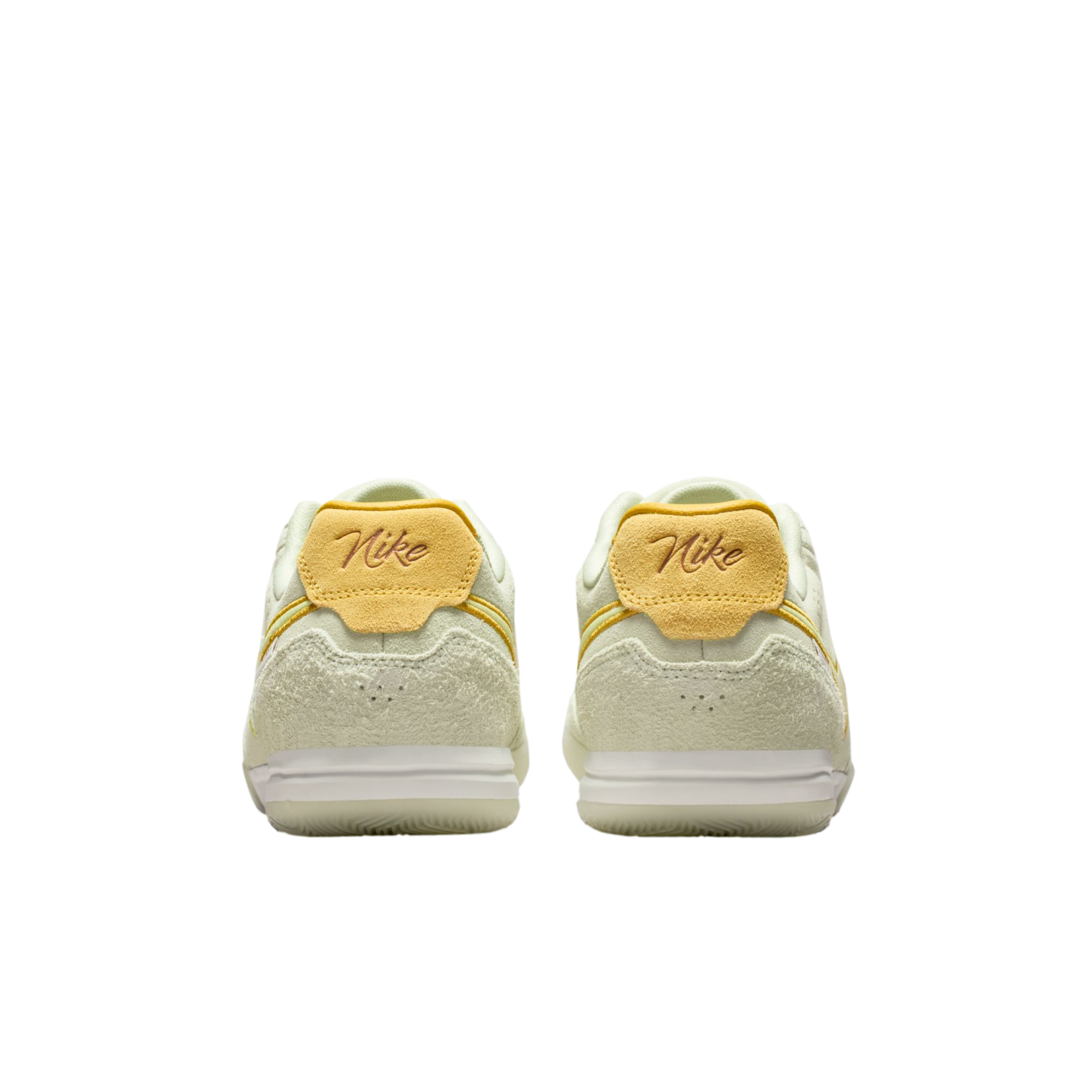 Rear view of a pair of light green Nike sneakers with yellow suede heel tabs, set against a black background.