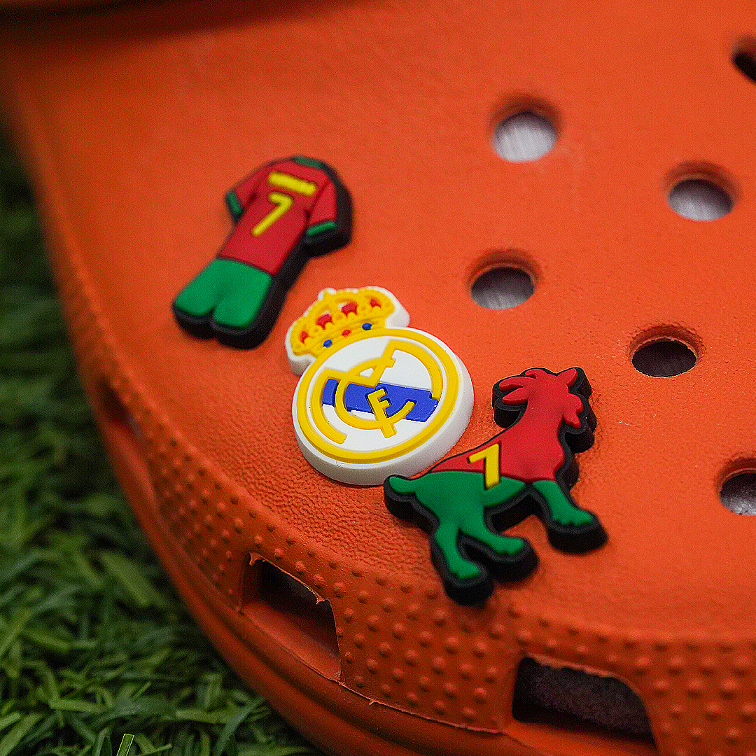 Soccer Croc Charm featuring three soccer-themed accessories—a Portugal jersey with the number 7, the Real Madrid crest, and a Portugal-colored GOAT emblem—plugged into the holes of an orange Croc shoe.