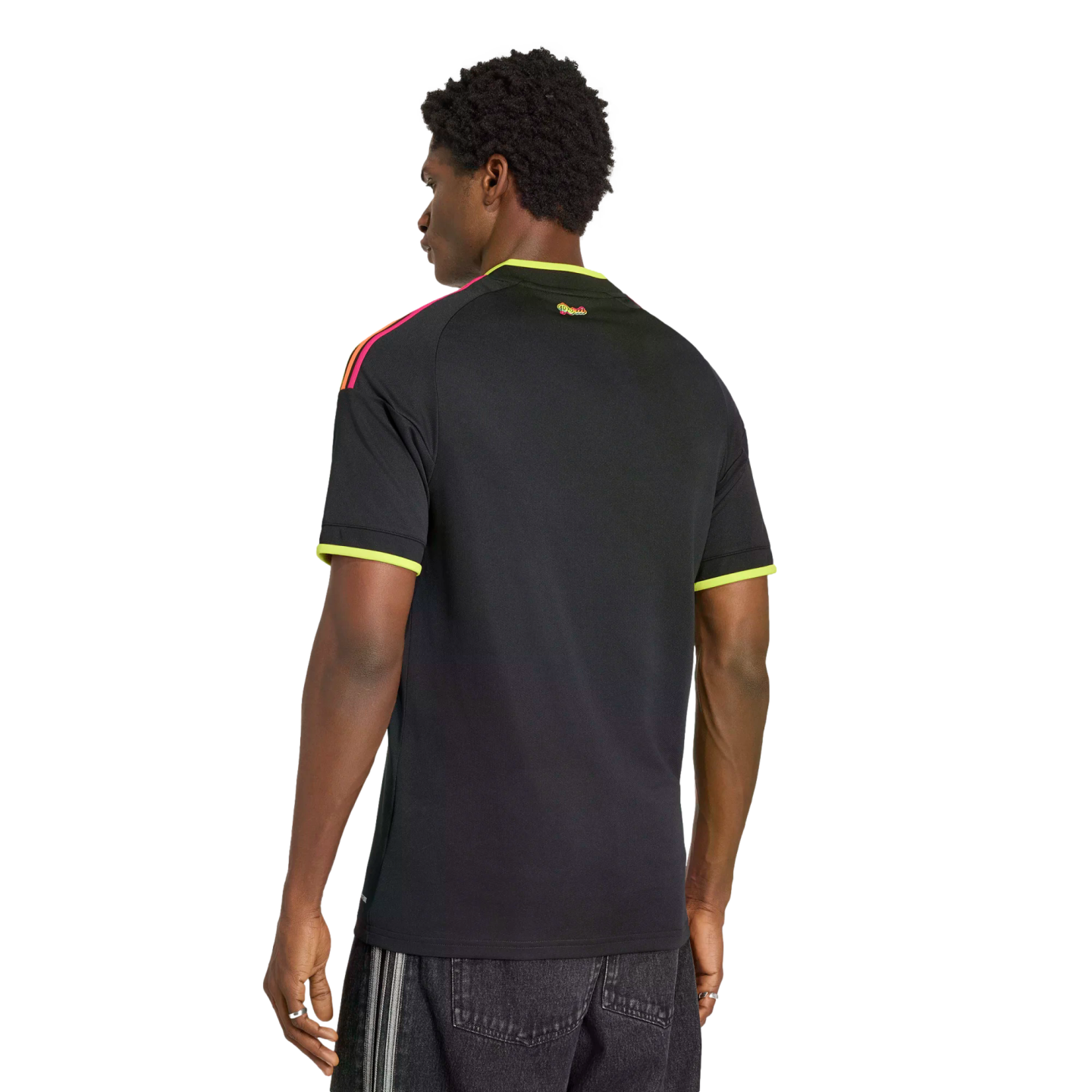 Rear view of a man wearing a black shirt with neon yellow trim and multi-colored shoulder stripes against a black background.