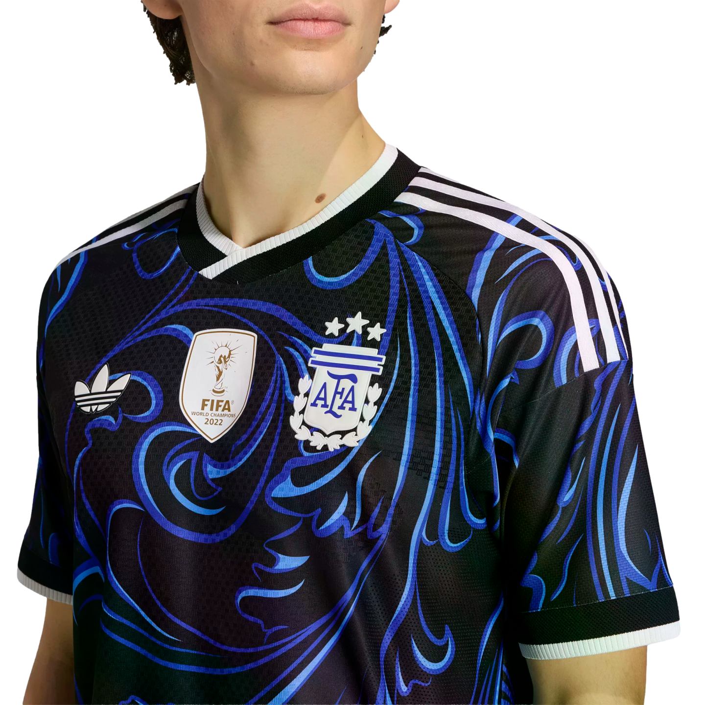 Person wearing a black Argentina soccer jersey with blue swirls, a 2022 FIFA World Champions patch, AFA crest with three stars, and white Adidas shoulder stripes.
