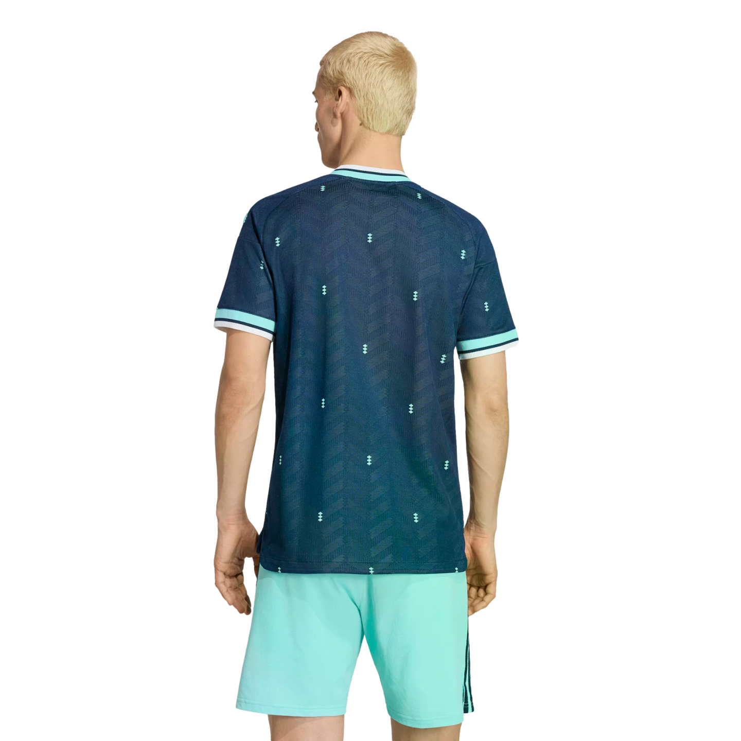 Rear view of a person with blonde hair in a patterned navy blue jersey and mint green athletic shorts, standing against a black background.