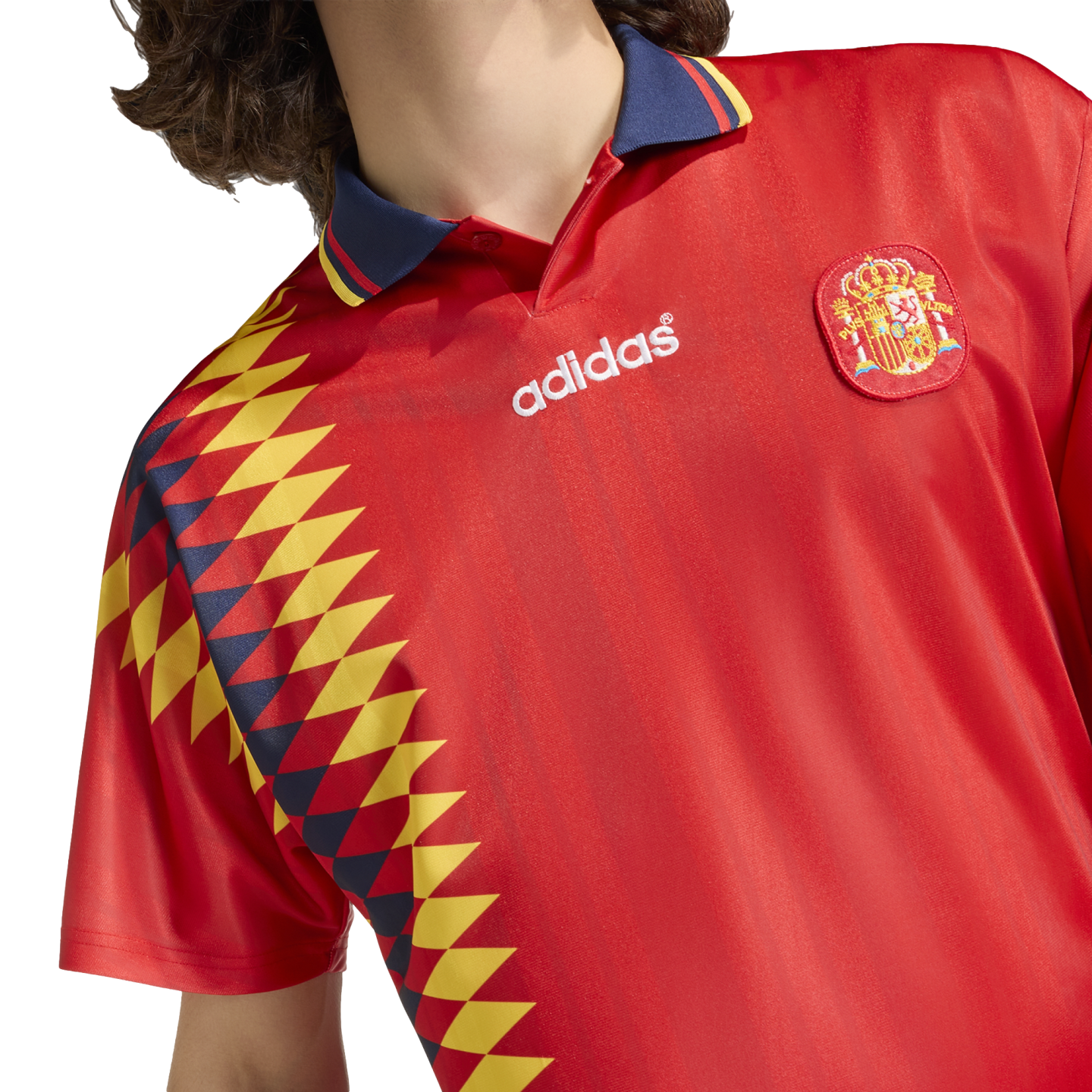 Red Spain Adidas football jersey with a blue polo collar, the national crest, and a vertical yellow and navy diamond pattern on the side.