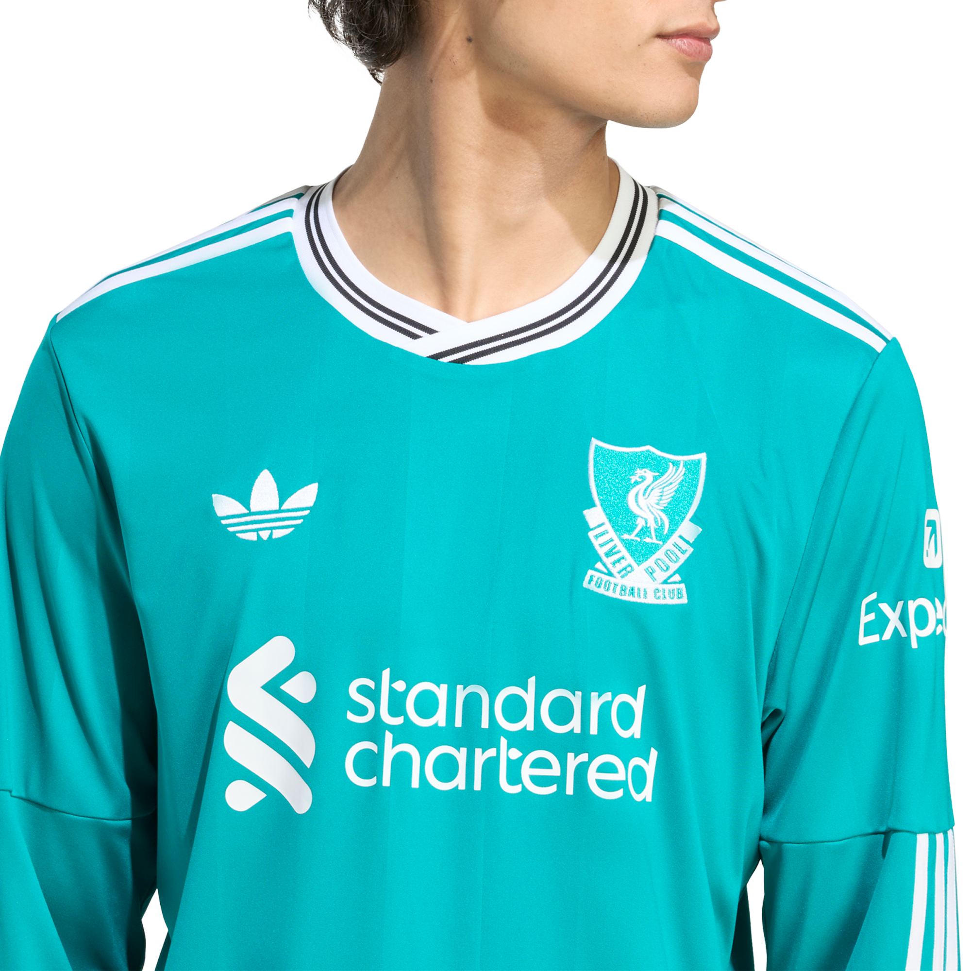 A person wearing a teal Liverpool FC long-sleeve jersey featuring white Adidas, Standard Chartered, and Expedia logos against a white background.