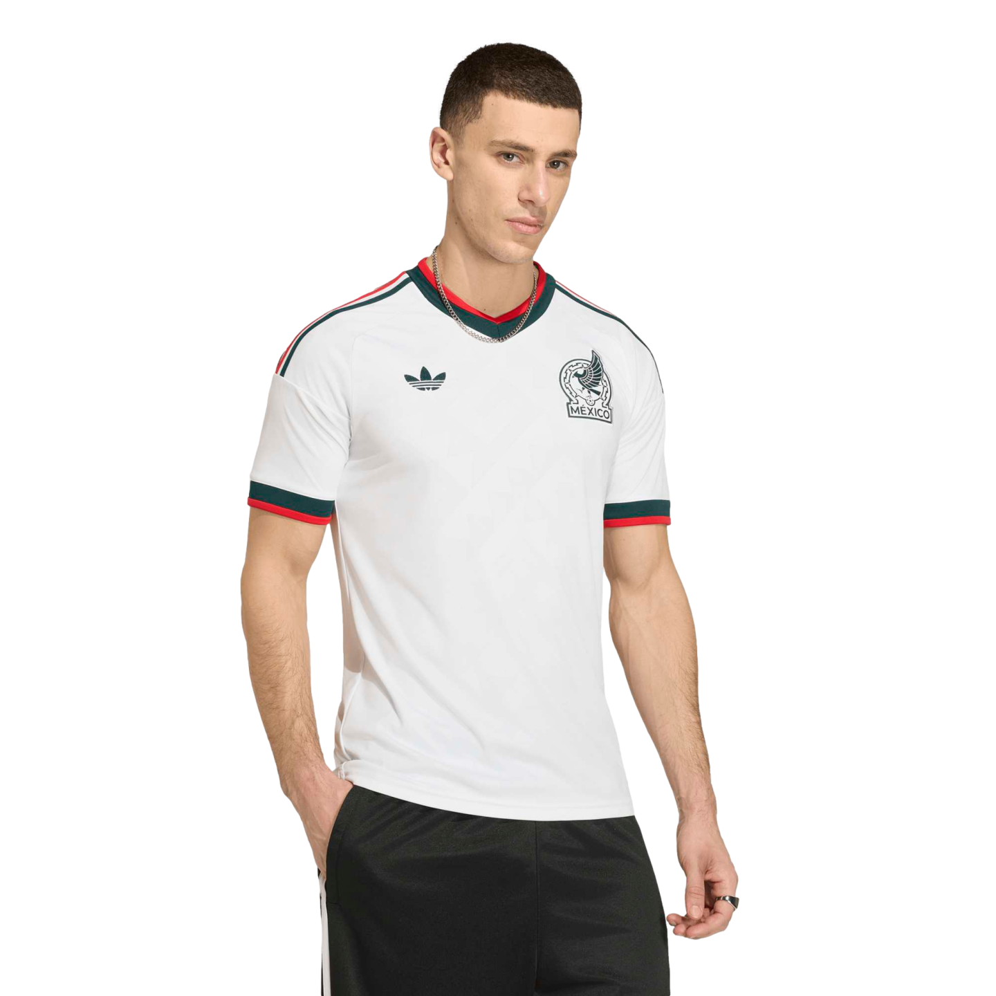 Man in a white Adidas Mexico soccer jersey with green and red trim, black shorts, and a silver chain against a black background.