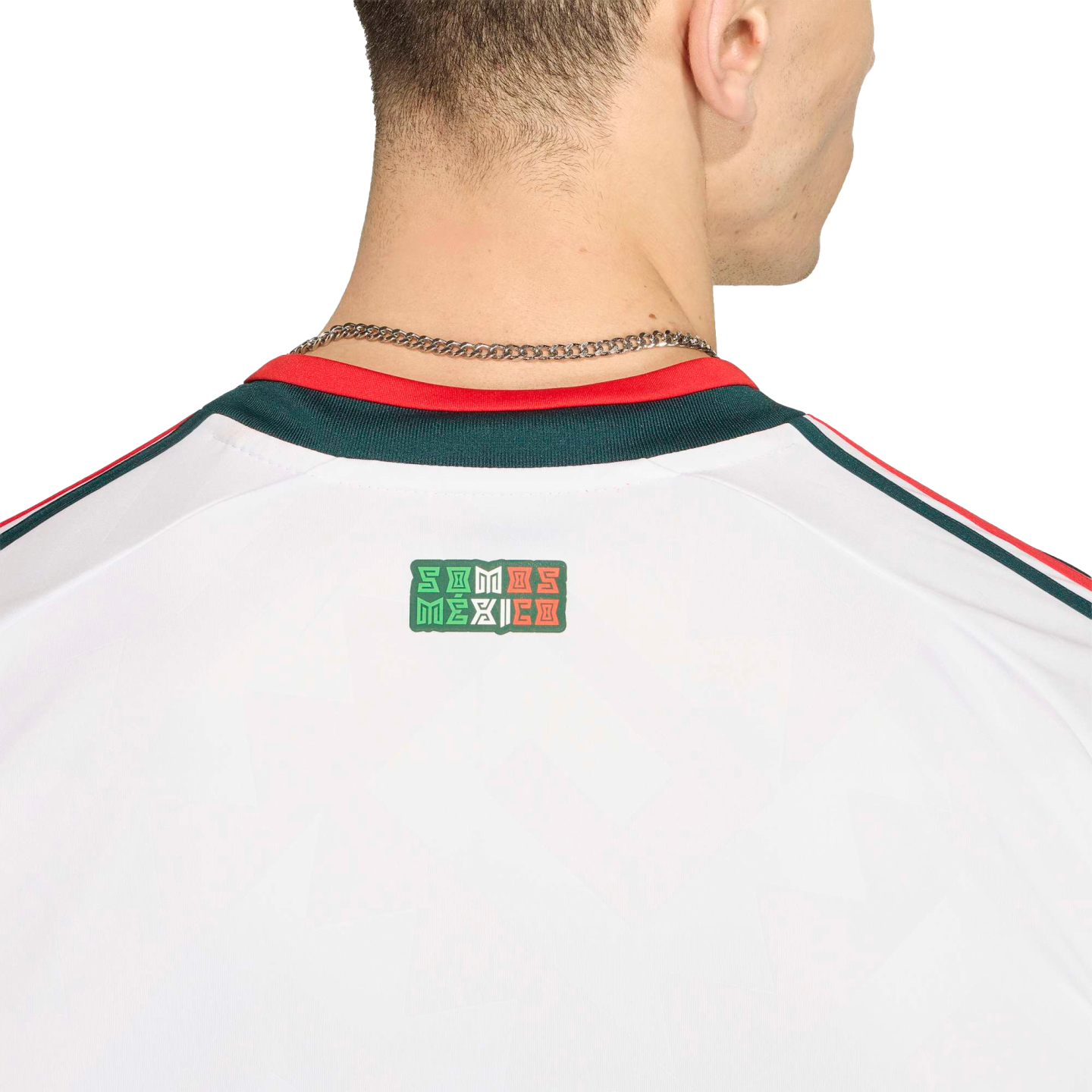 Close-up of the back of a white jersey with a 'SOMOS MÉXICO' logo and a red and green collar. A silver chain necklace is visible on the person's neck against a black background.