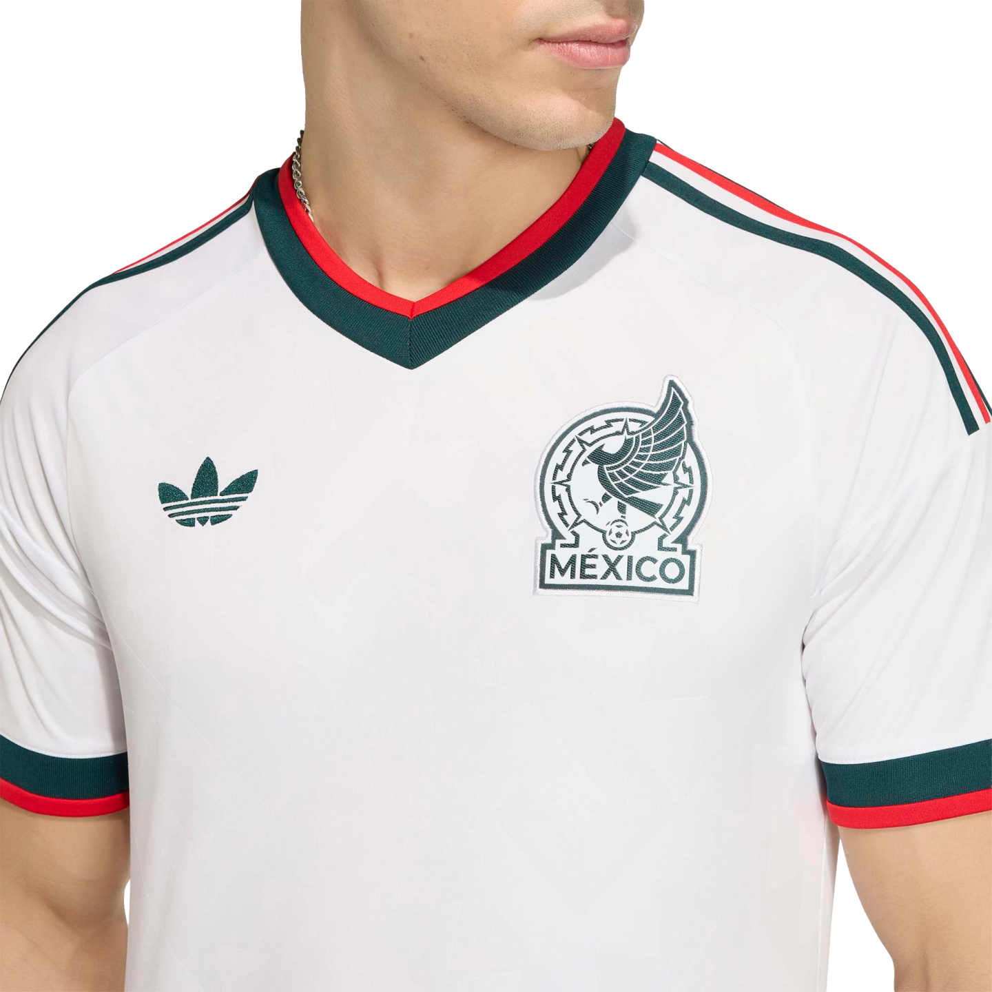 Close-up of a white Mexico national team soccer jersey featuring green and red trim, the team crest, and a green Adidas logo.