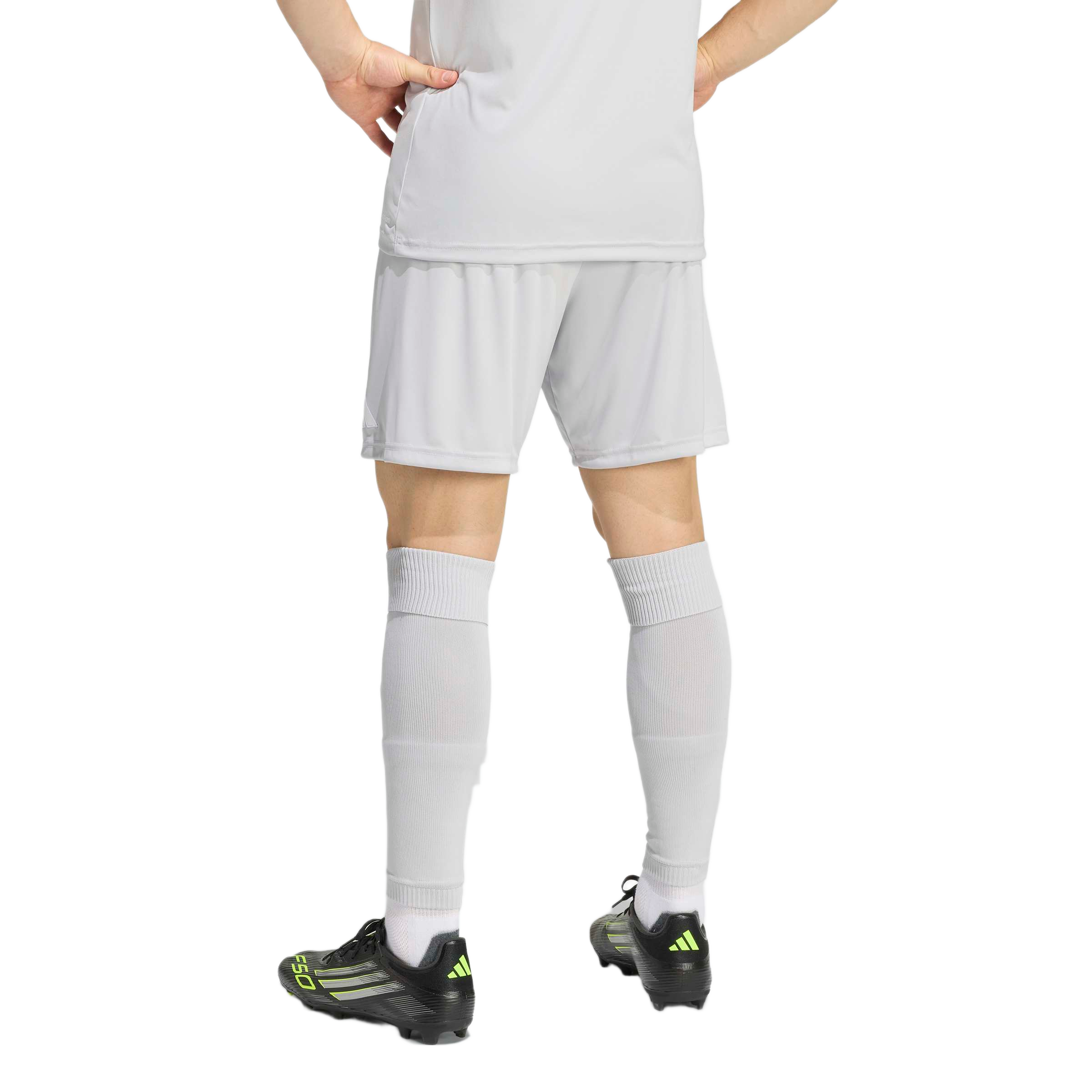 Back view of a person wearing a light gray soccer kit and black Adidas cleats with neon yellow accents.