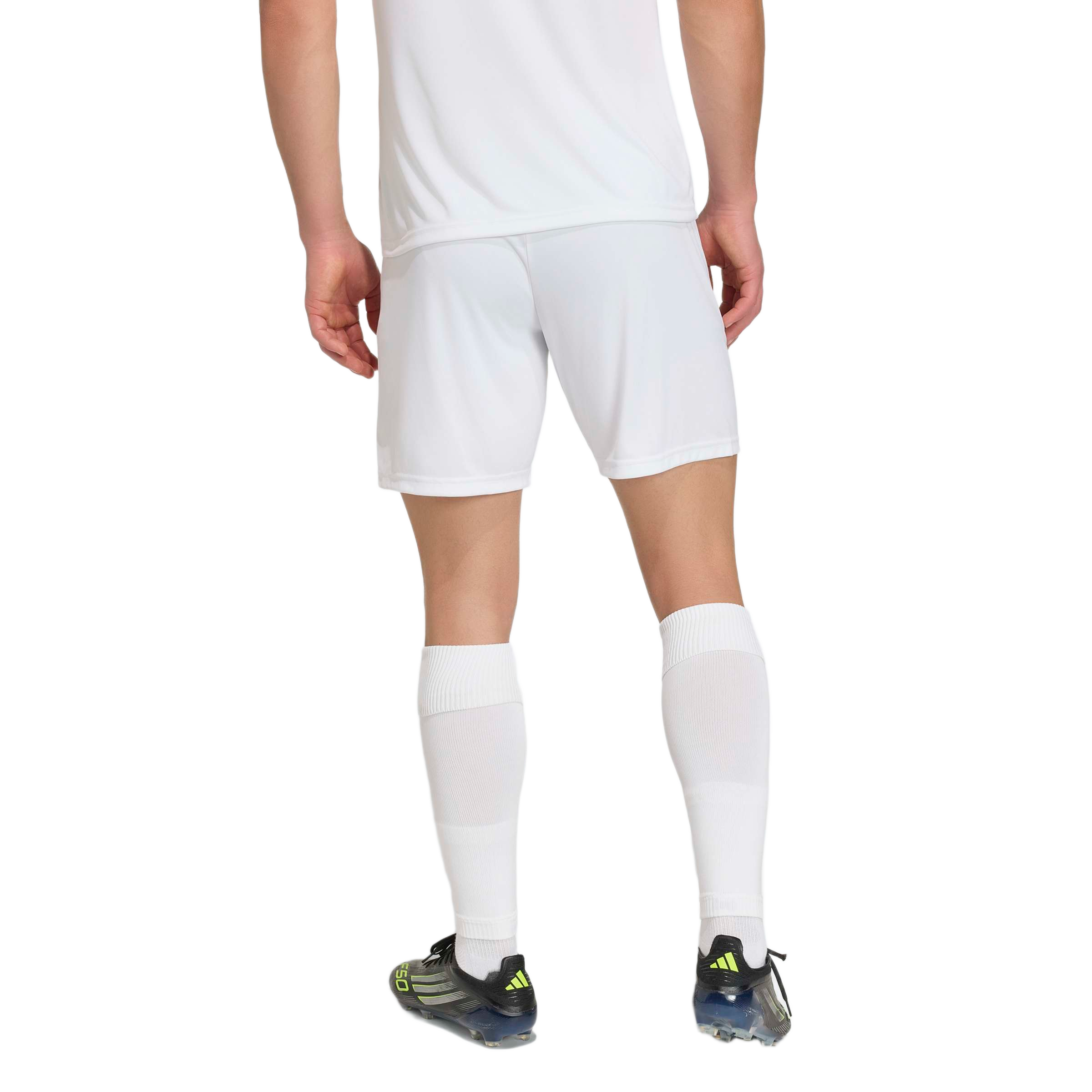 Back view of a person in white soccer shorts and socks, wearing black and lime green cleats against a light gray background.