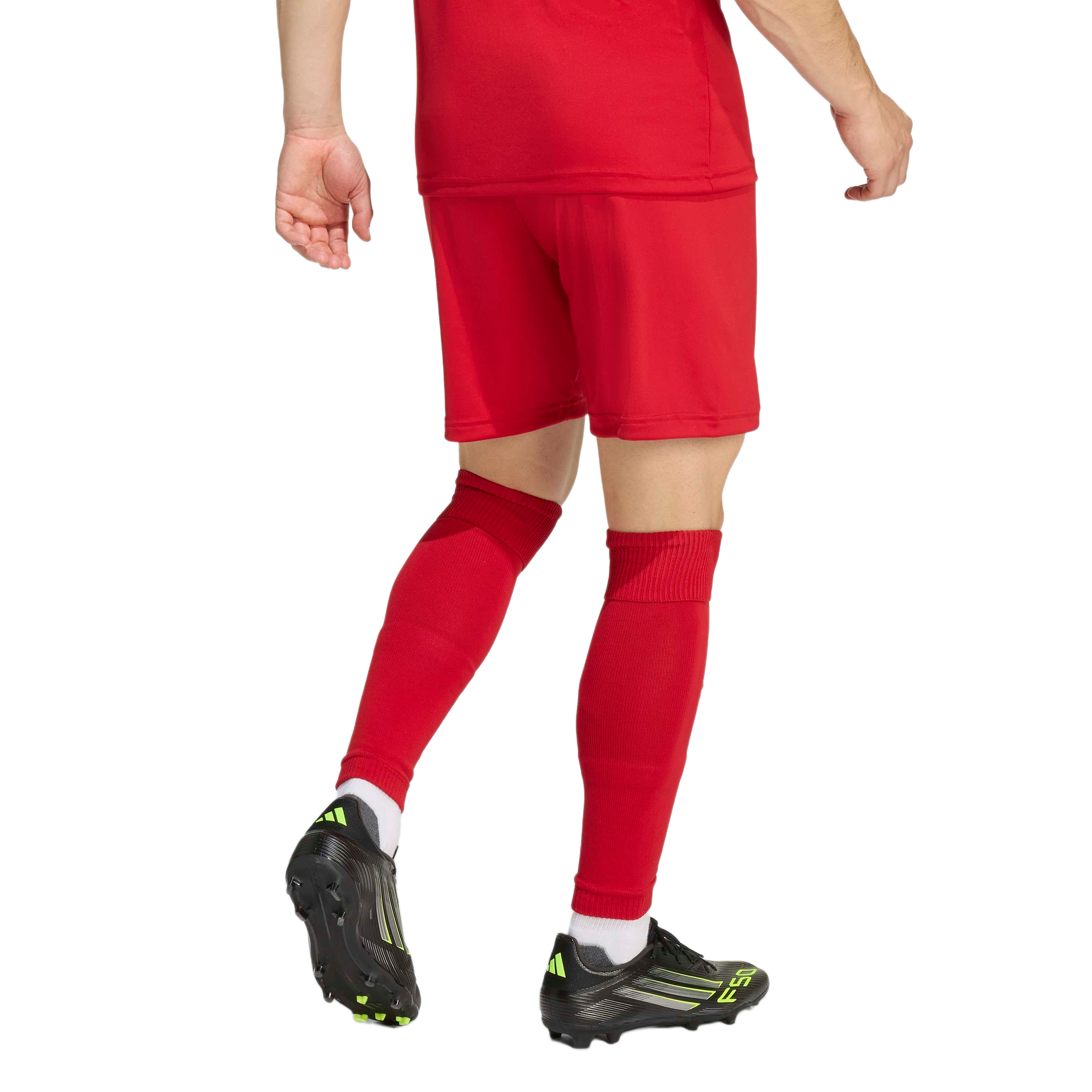 Rear view of a person wearing a red soccer jersey, shorts, and socks with black and lime green soccer cleats against a white background.