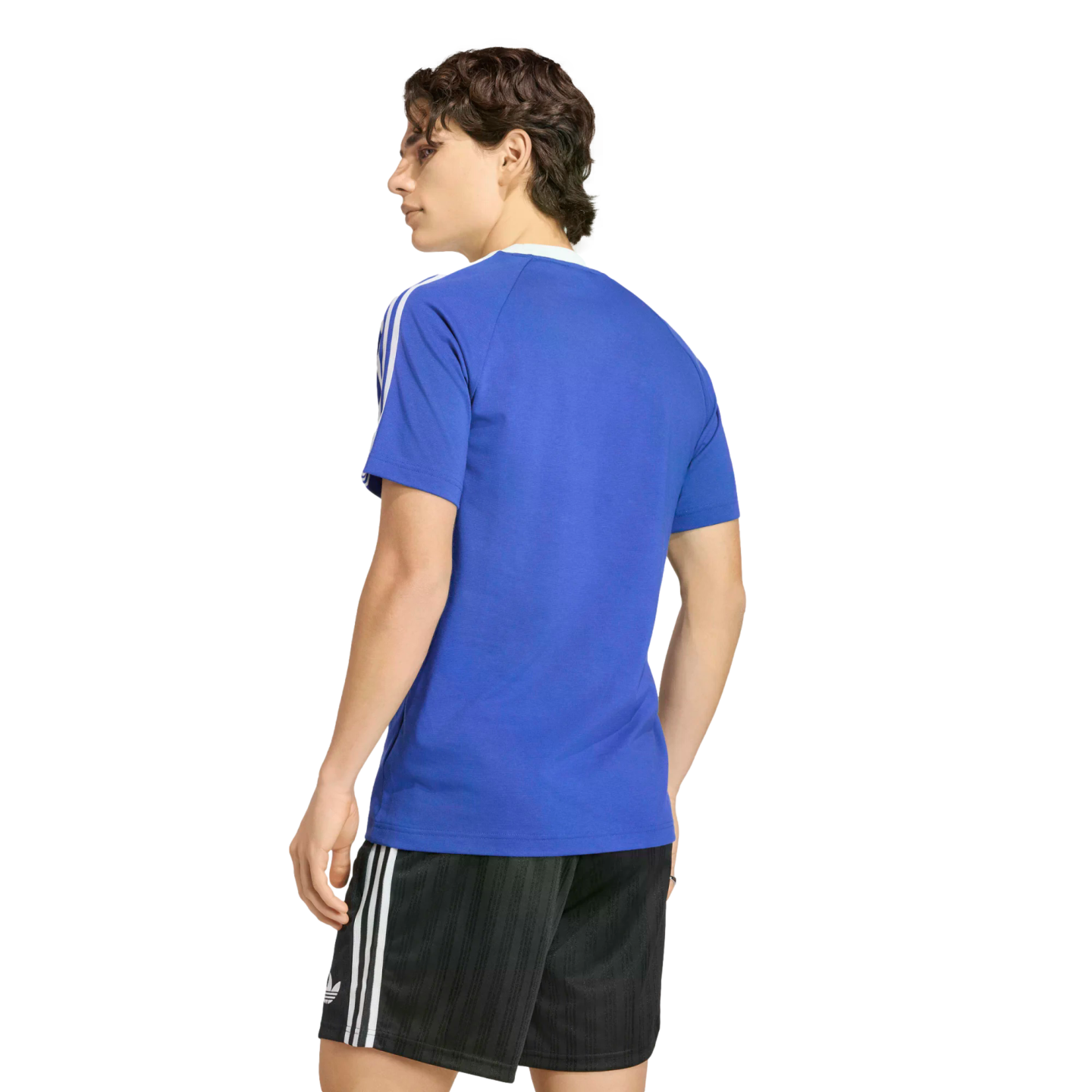 A rear view of a person with wavy brown hair wearing a blue t-shirt with white stripes on the sleeves and black athletic shorts with white stripes, standing against a solid black background.