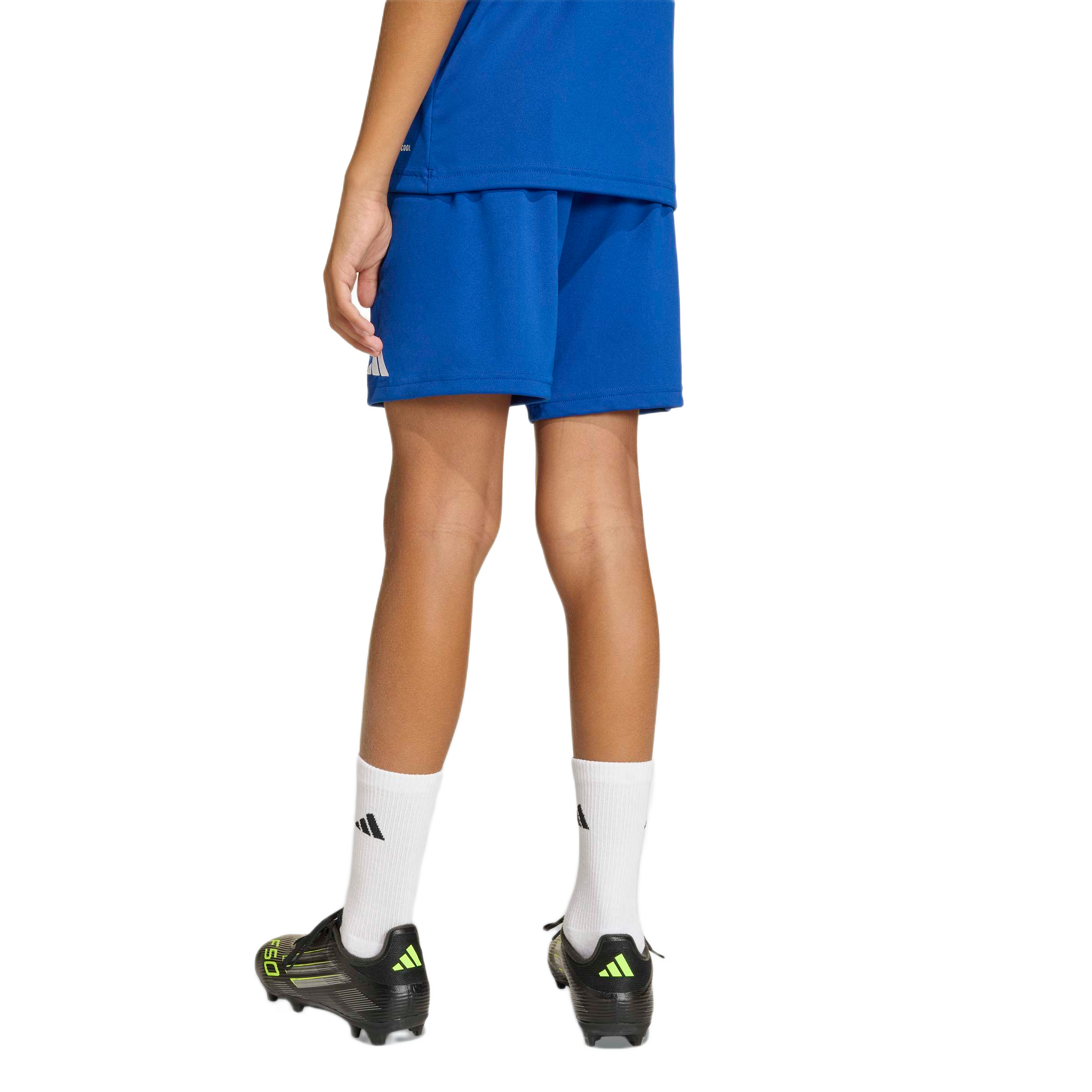 Back view of a youth wearing a blue athletic kit, white socks, and black Adidas soccer cleats with yellow accents.