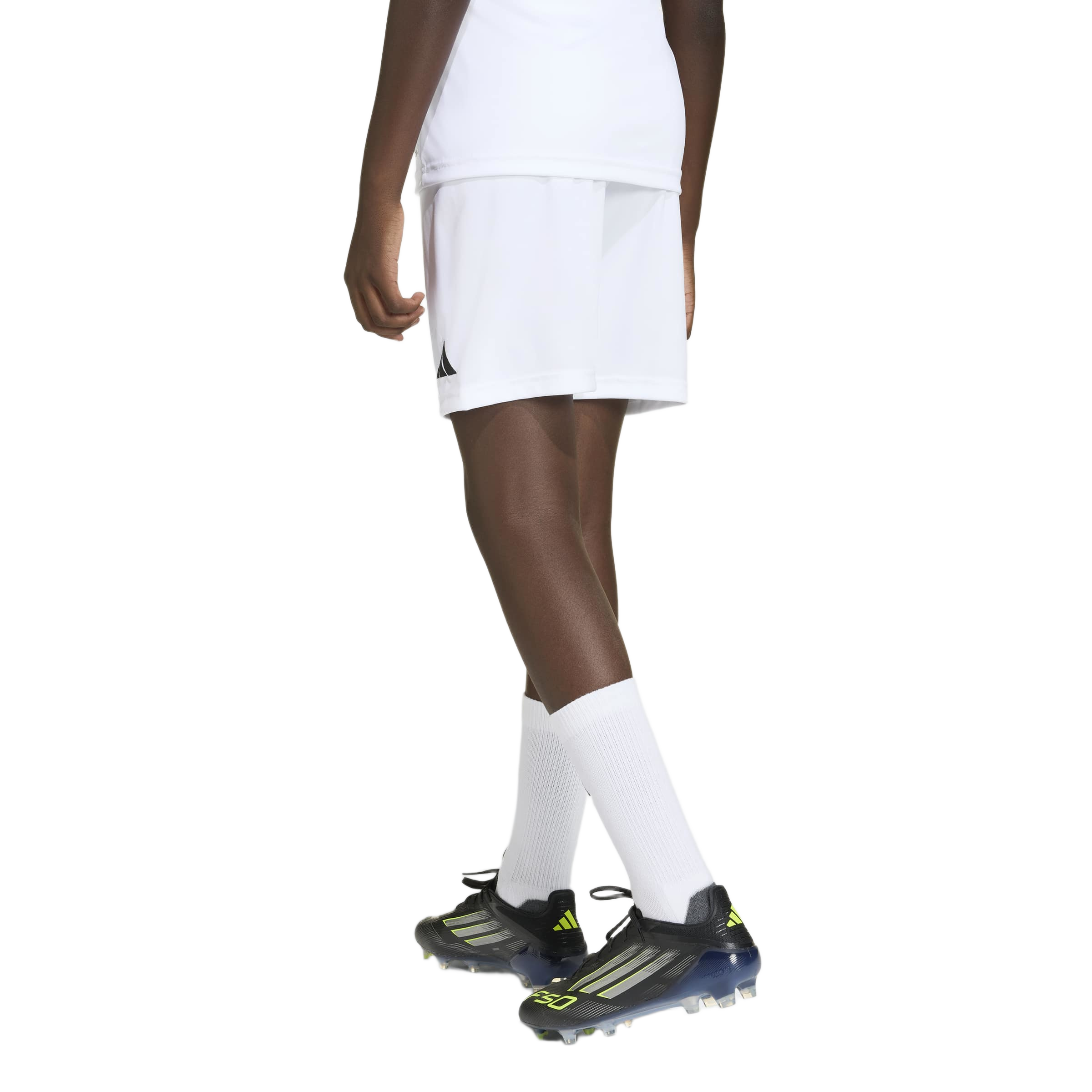 Rear view of a person from the waist down wearing a white soccer uniform and black cleats against a plain gray background.