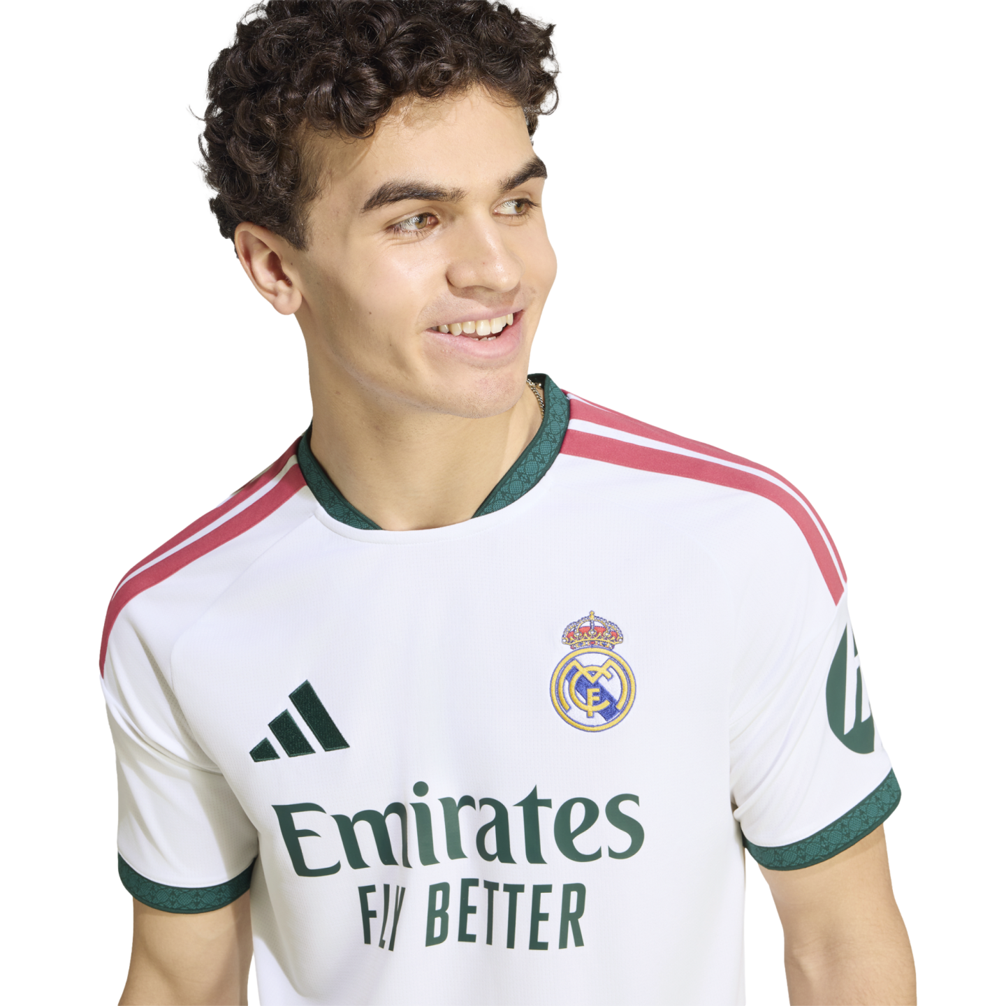 Smiling young man with curly hair wearing a white Real Madrid soccer jersey with green and pink accents.