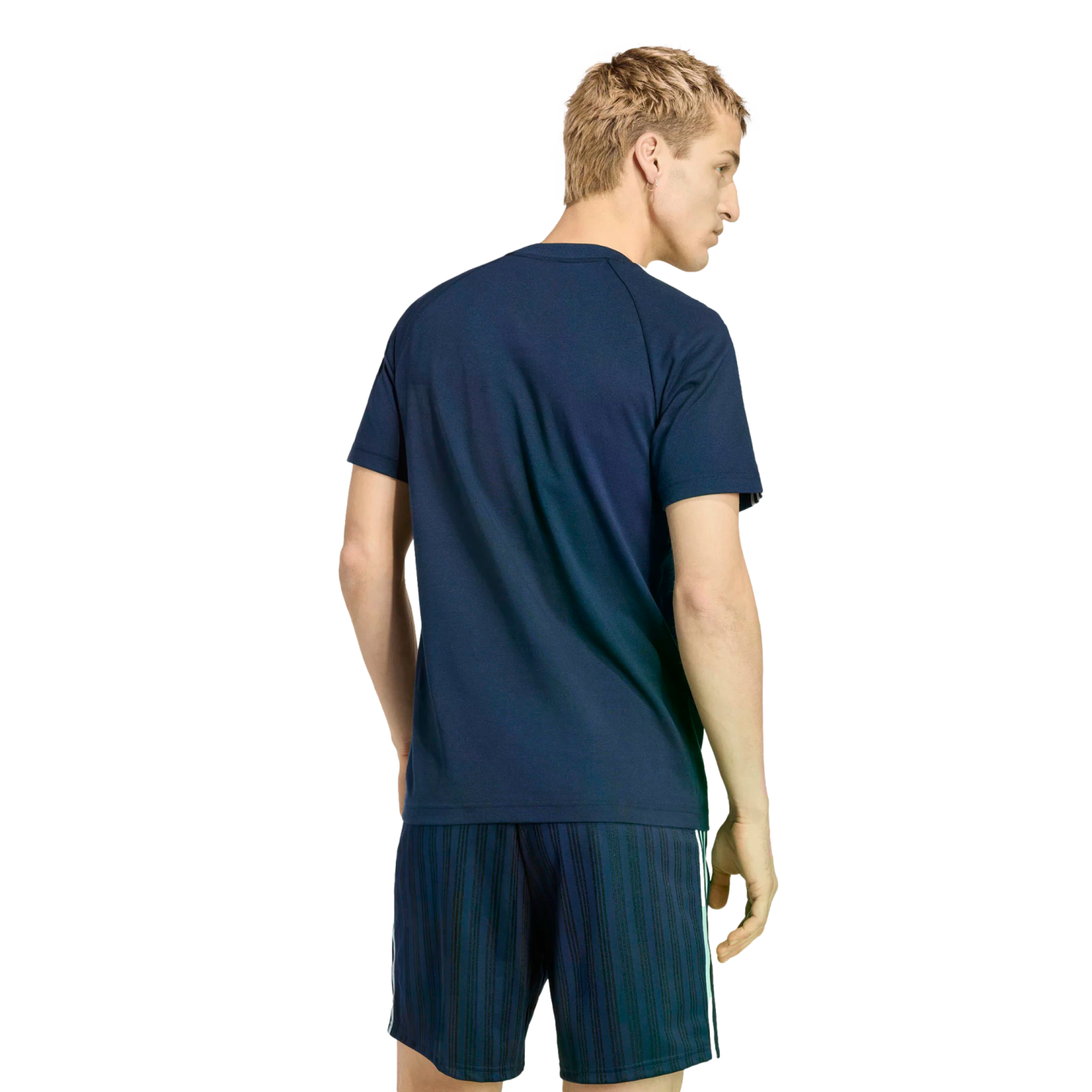 Back view of a man with blonde hair wearing a navy blue t-shirt and matching striped shorts against a black background.