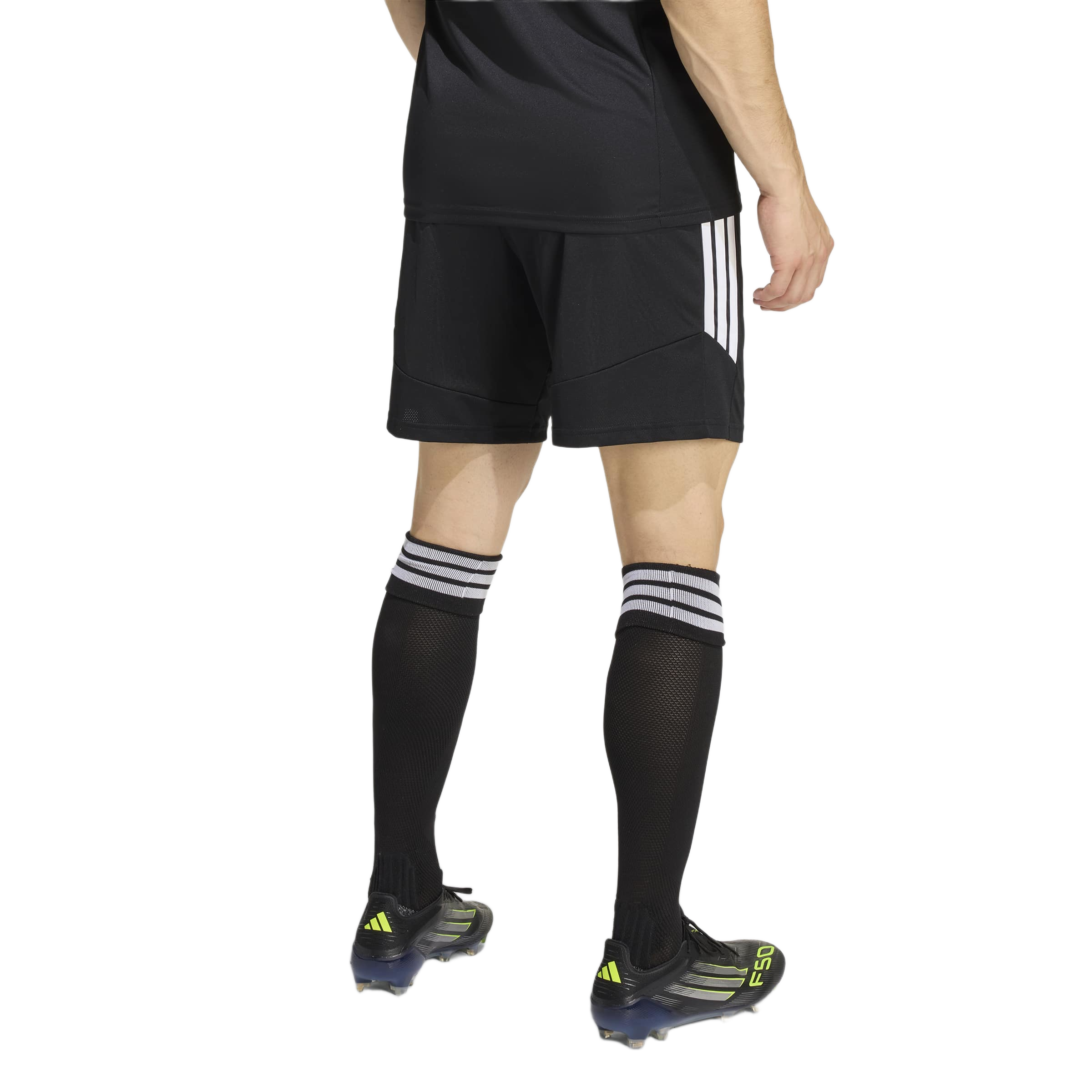 Rear view of a person wearing black Adidas soccer shorts and knee-high socks with three white stripes, and black cleats with neon yellow accents.