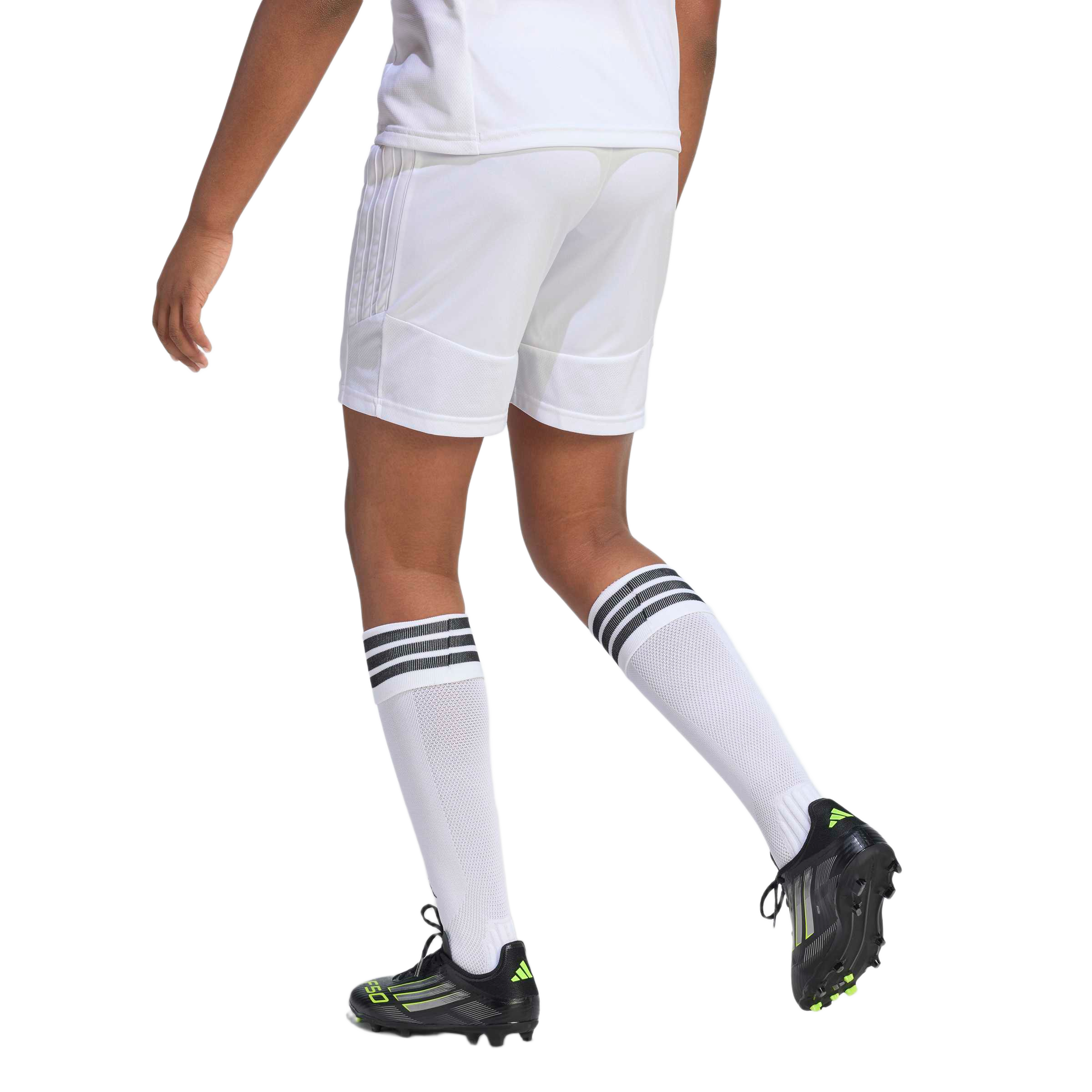 Rear view of an athlete in motion wearing a white soccer uniform, striped knee-high socks, and black cleats on a light gray background.