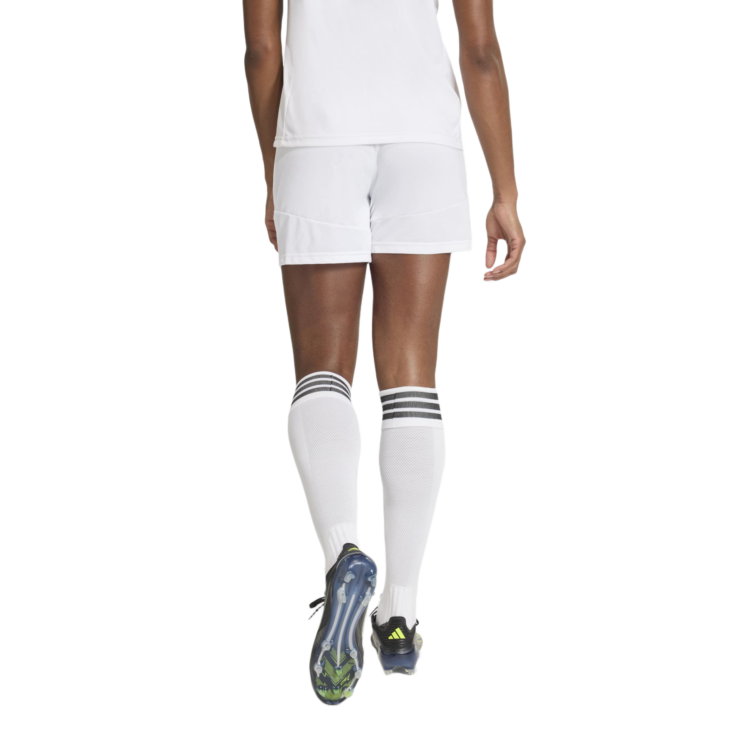 Rear view of a person wearing a white soccer kit with knee-high socks and black cleats, walking away against a gray background.