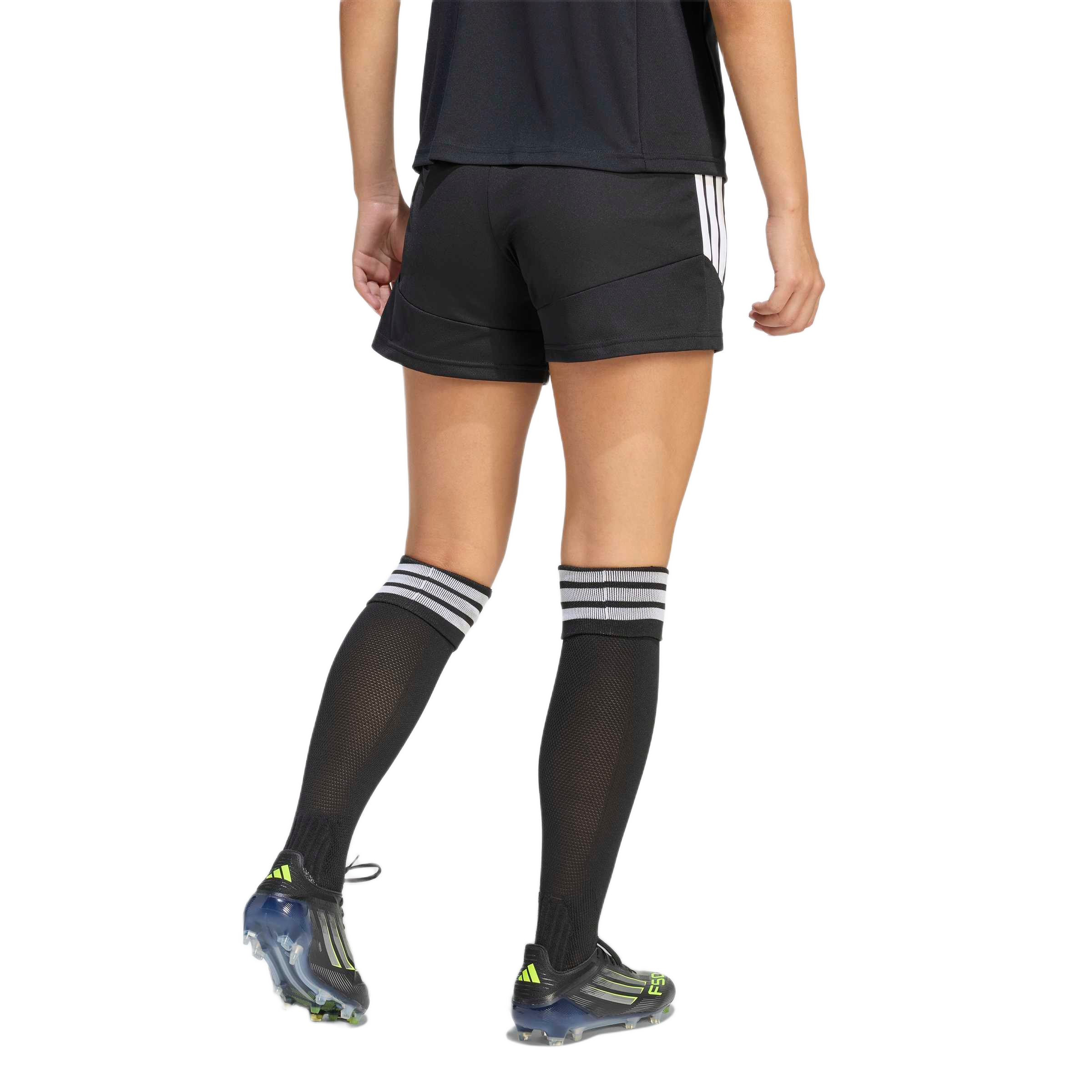 Rear view of a person wearing black soccer shorts, knee-high black socks with white stripes, and black soccer cleats with yellow accents.