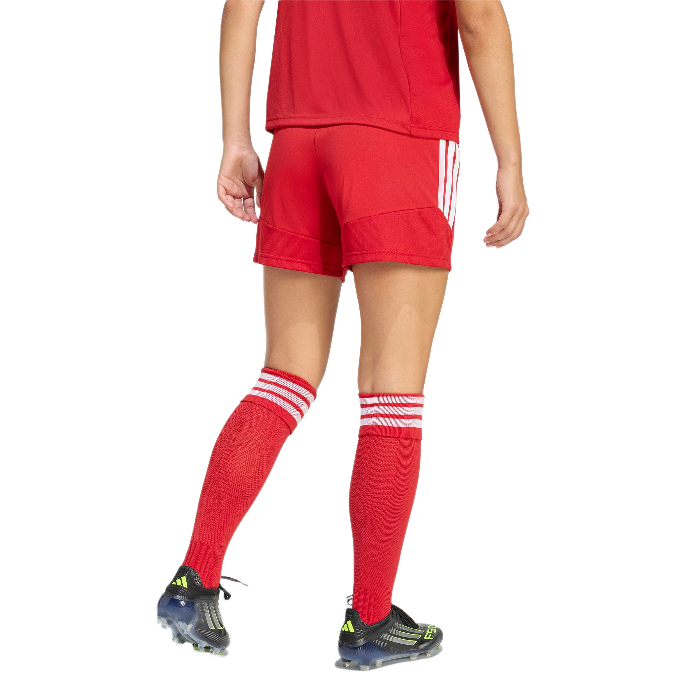 Rear view of a person wearing a red soccer kit featuring shorts, knee-high striped socks, and black soccer cleats against a light grey background.