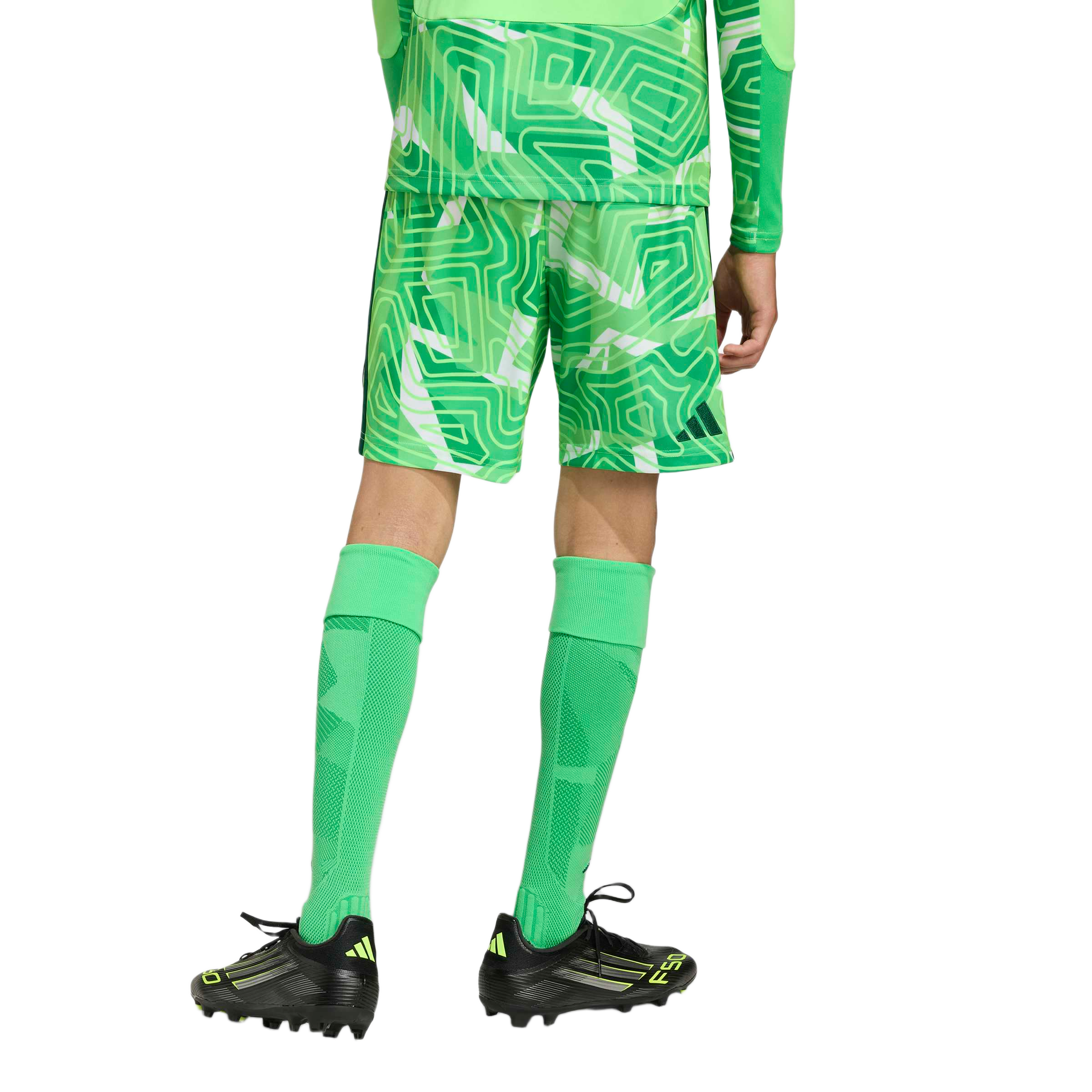 Rear view of a person wearing a green patterned soccer kit, tall green socks, and black and neon yellow soccer cleats against a light gray background.