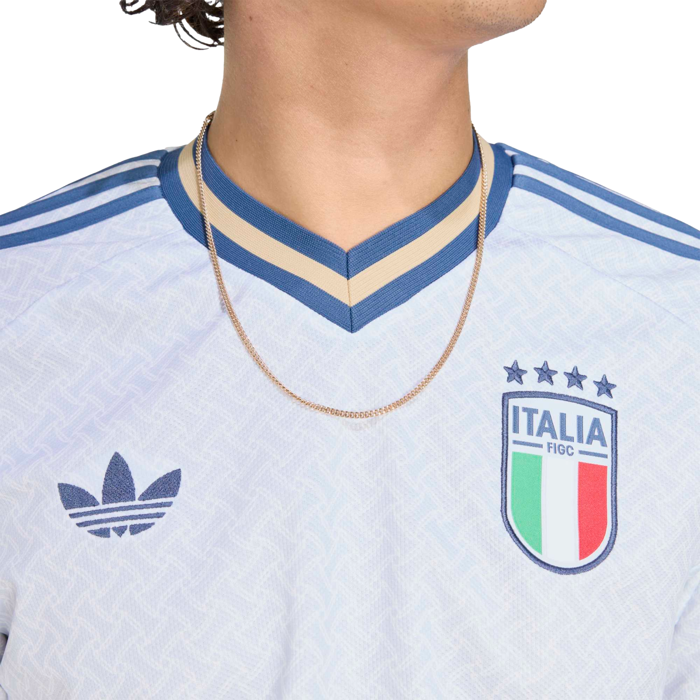 Close-up of a white Adidas Italy national team jersey featuring the FIGC crest, blue trefoil logo, and a blue and tan striped V-neck collar.