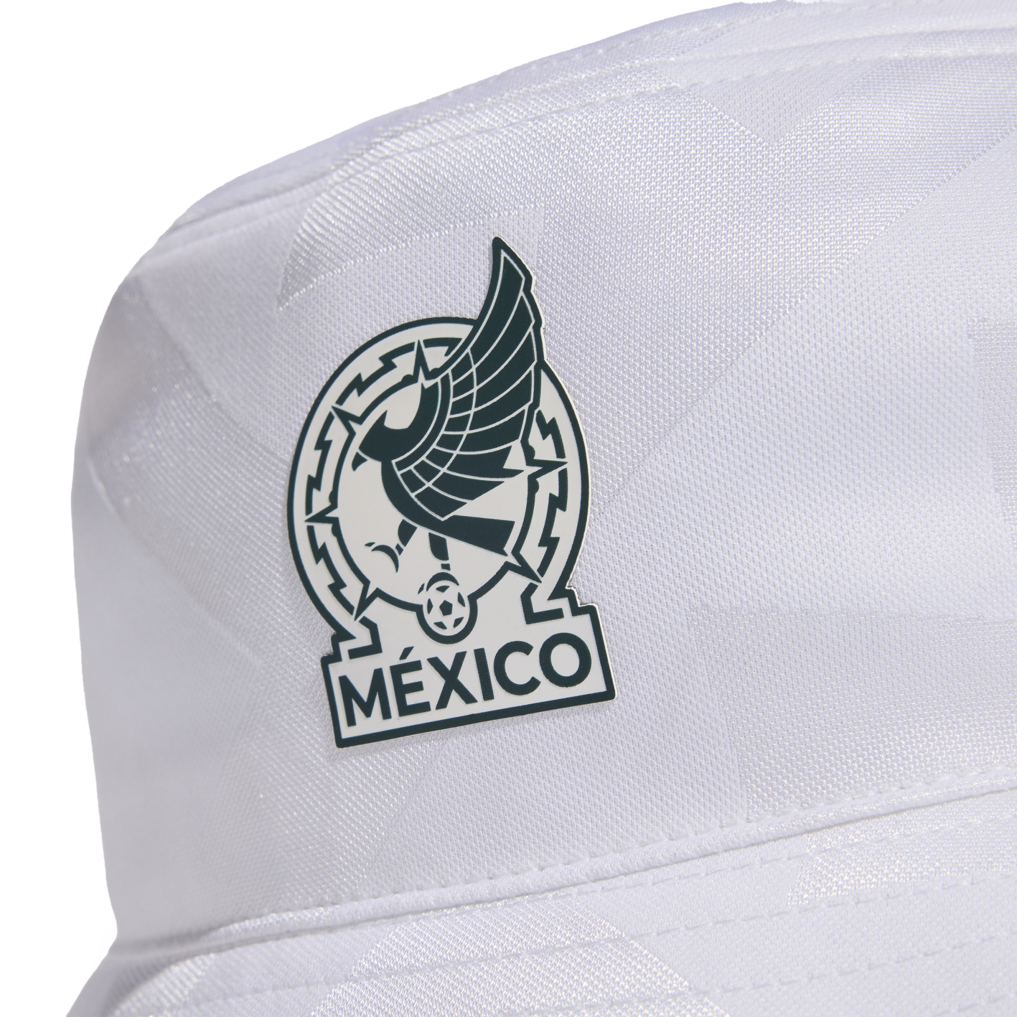 A close-up of a white bucket hat featuring a dark green and white patch. The patch depicts a stylized Aztec eagle, a soccer ball, and the word "MÉXICO" at the bottom.