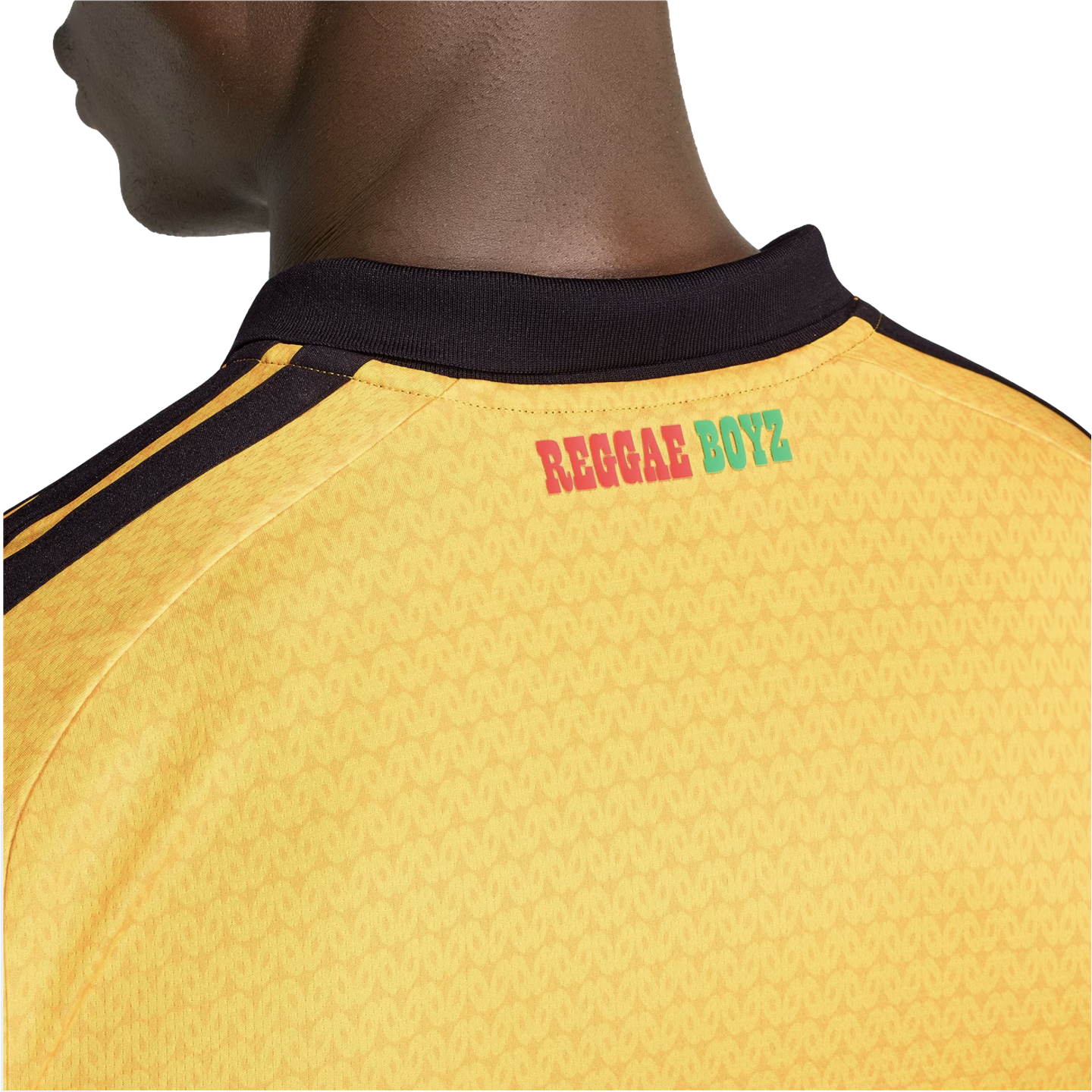 Close-up of the back of a yellow jersey with black stripes on the shoulders and "REGGAE BOYZ" printed in red and green below a black collar.