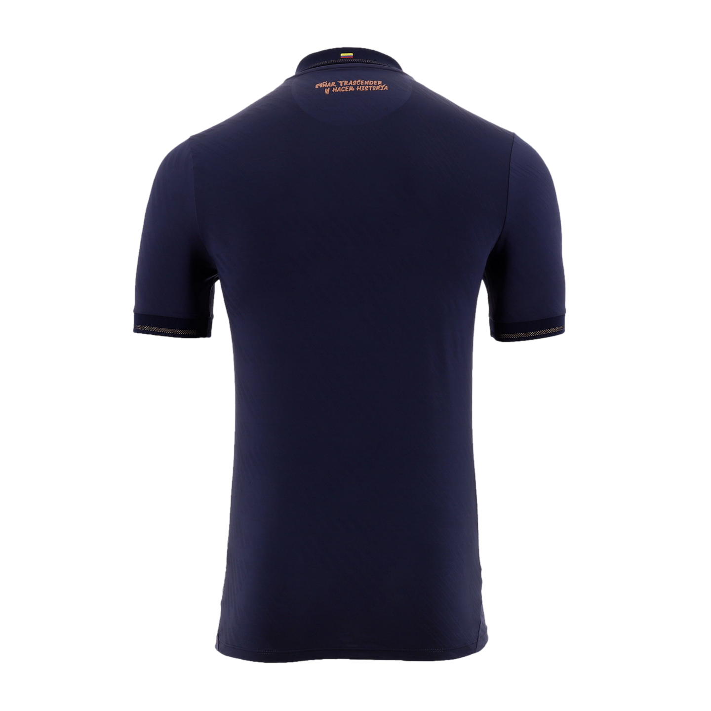 A back view of a navy blue short-sleeved soccer jersey against a solid black background. Near the collar, there is a small Colombian flag above the copper-colored Spanish text, "SOÑAR TRASCENDER Y HACER HISTORIA." The sleeve cuffs are accented with a matching copper-colored trim.