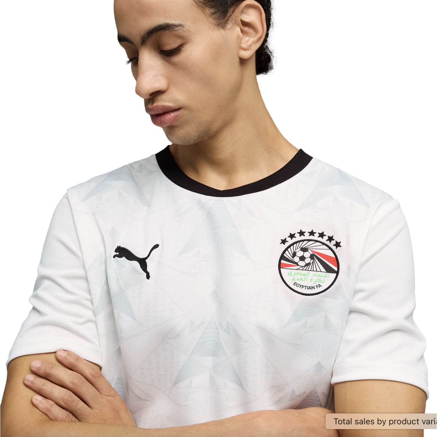 A young man looks down with his arms crossed, wearing a white Puma soccer jersey with a black crew neck and a subtle geometric pattern. The jersey features the Egyptian Football Association crest on the left chest and a black Puma logo on the right, all set against a solid black background.