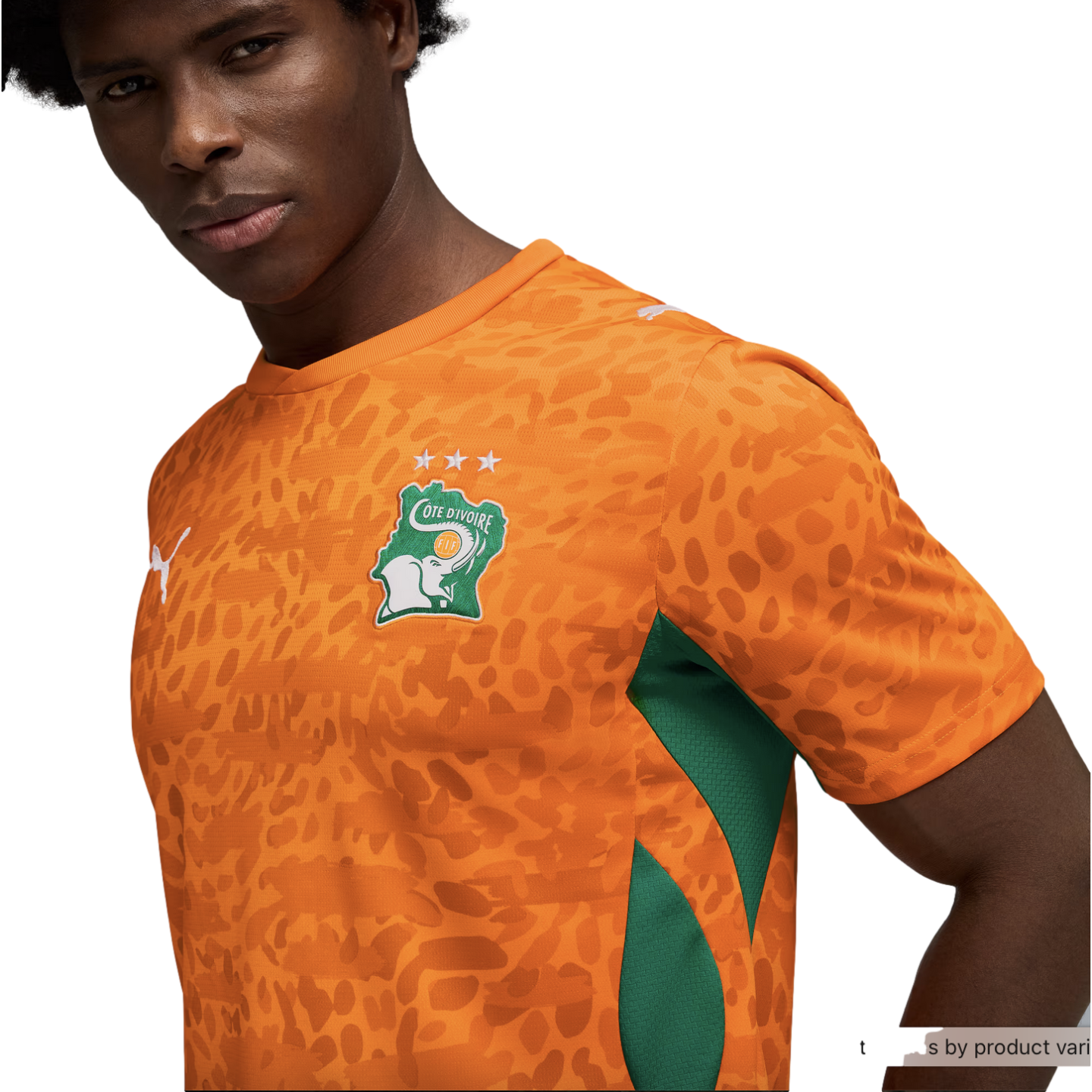 A close-up of a man wearing an orange Côte d'Ivoire national football team jersey against a black background. The jersey features a tonal animal-print pattern, green mesh panels on the sides, and the team's crest on the chest, which includes a white elephant and three stars above it. A white Puma logo is visible on the chest and sleeve.