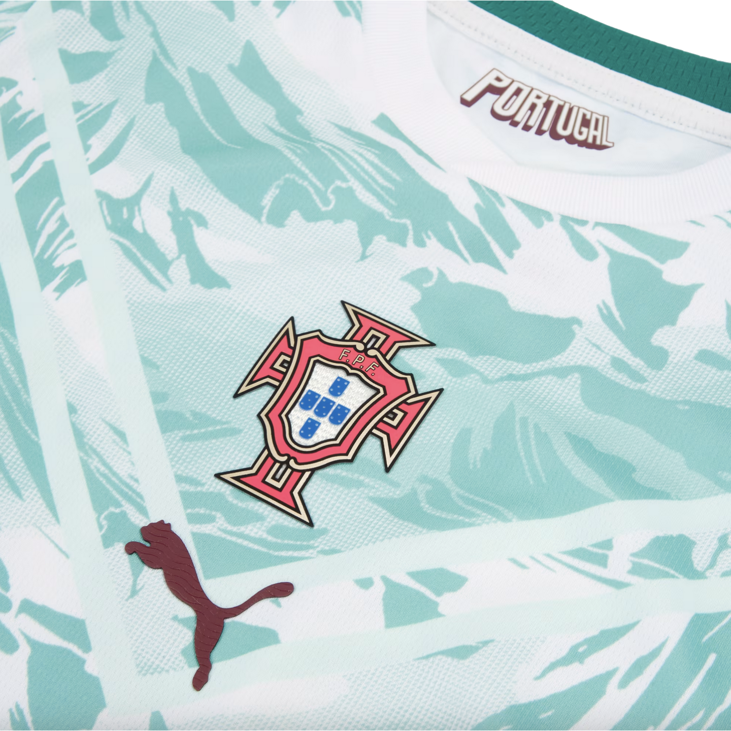 A close-up of a Portugal national football team jersey, featuring a light mint green and white marbled pattern. The central focus is the Portuguese Football Federation (FPF) crest. A dark red Puma logo is positioned to the bottom left, and the word "PORTUGAL" is printed inside the collar. Two white diagonal stripes form a 'V' shape behind the logos.