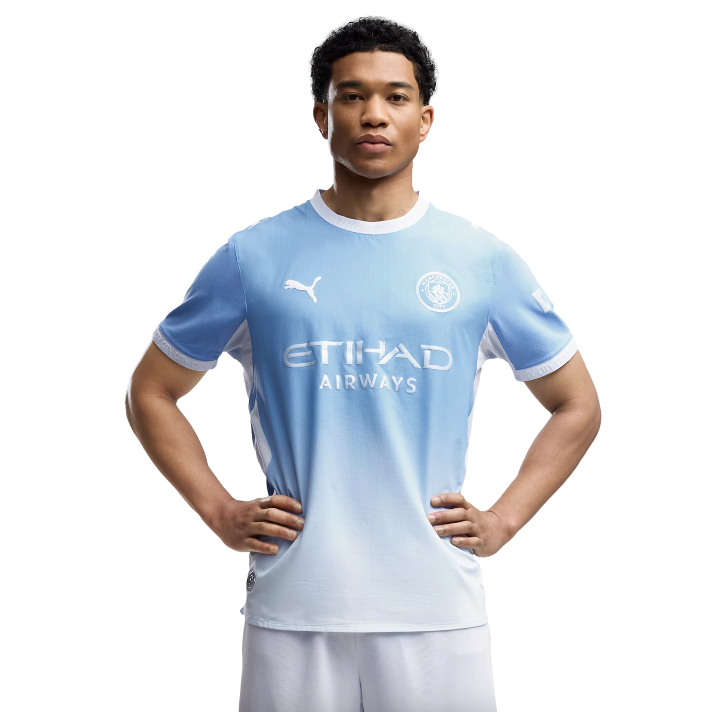 A young man wearing a light blue Manchester City soccer kit poses with his hands on his hips against a white background.