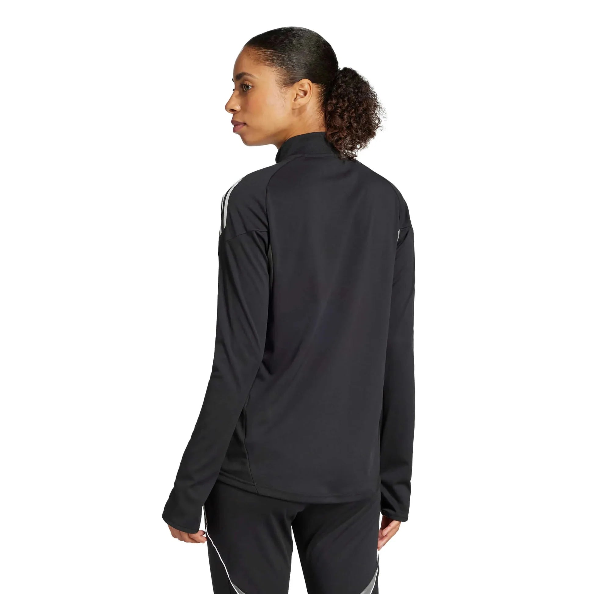 A woman from the back wearing a black athletic top and pants with white stripes. She has a curly ponytail and looks sideways against a plain white background.
